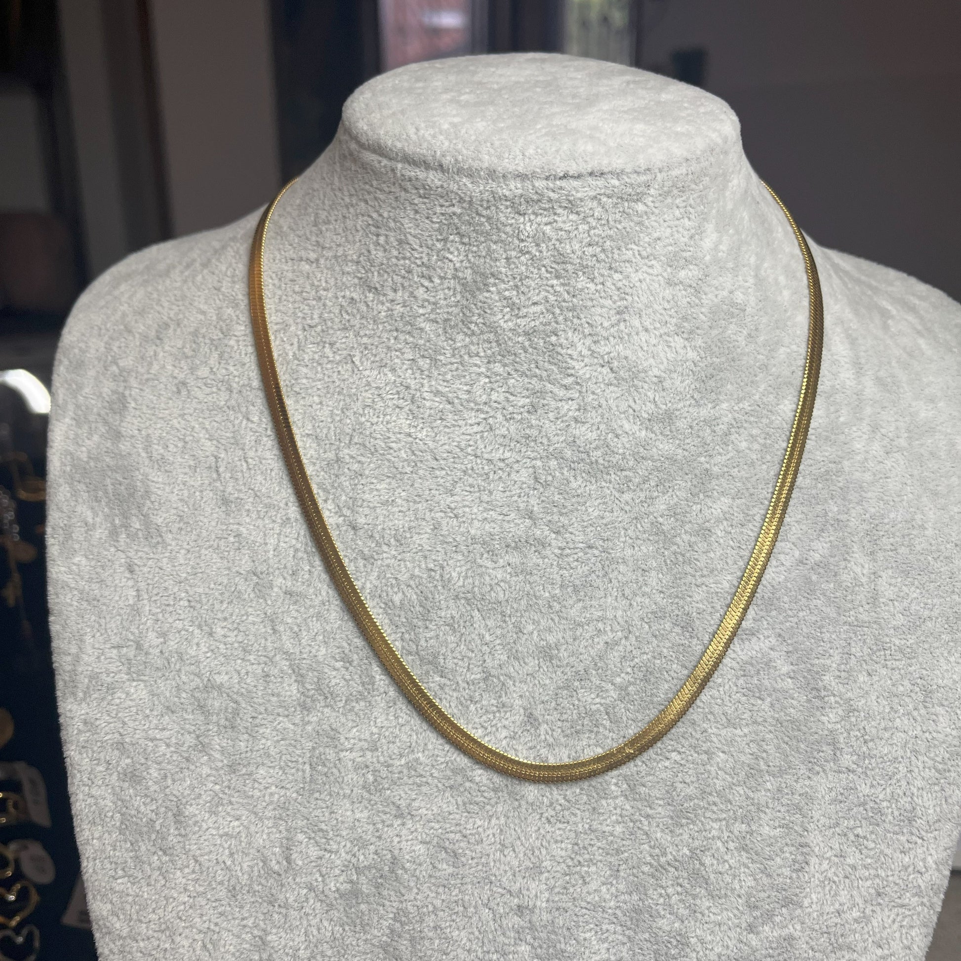 Collana Snake in acciaio premium in placcatura argento, con design ultra-sottile fluido, esposta su busto grigio chiaro