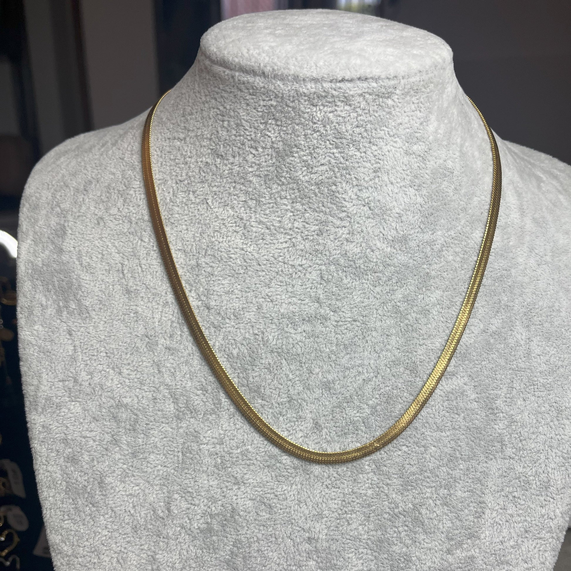 Collana Snake in acciaio premium in placcatura argento, con design ultra-sottile fluido, esposta su busto grigio chiaro