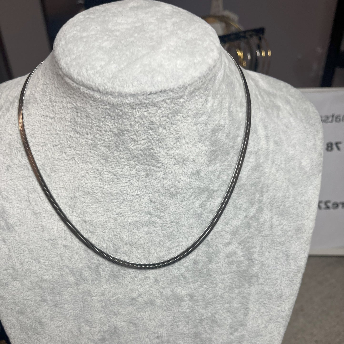 Collana Snake in acciaio premium in placcatura argento, con design ultra-sottile fluido, esposta su busto grigio chiaro