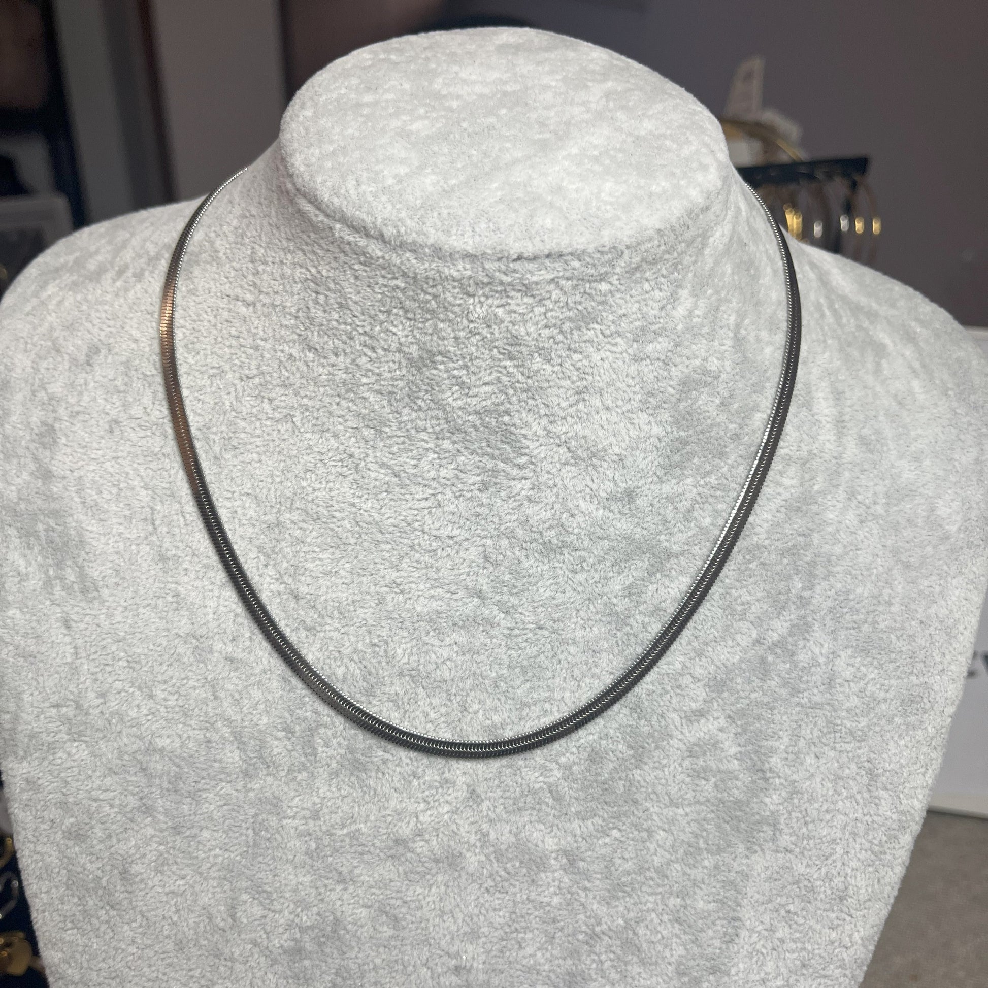 Collana Snake in acciaio premium in placcatura argento, con design ultra-sottile fluido, esposta su busto grigio chiaro