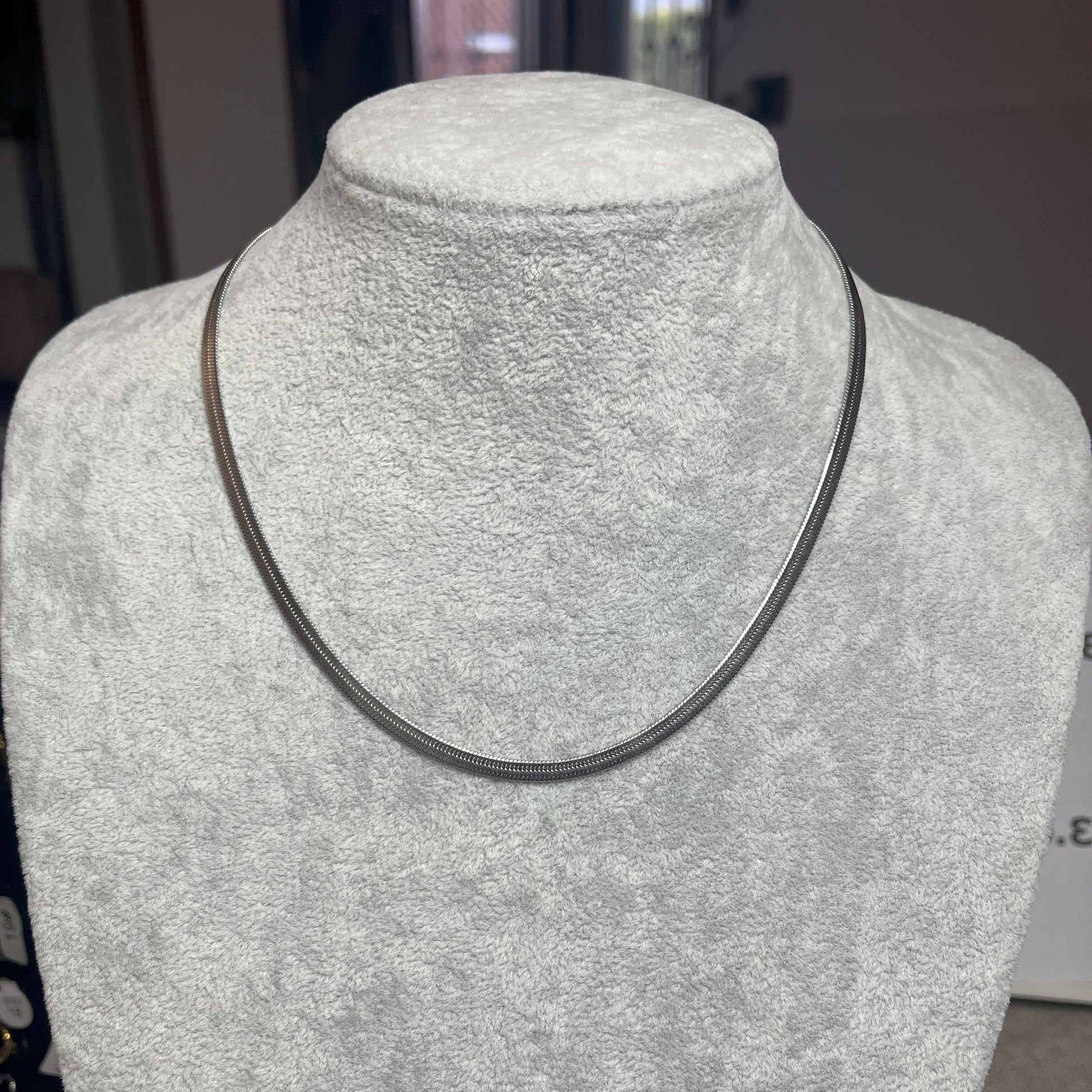 Collana Snake in acciaio premium in placcatura argento, con design ultra-sottile fluido, esposta su busto grigio chiaro