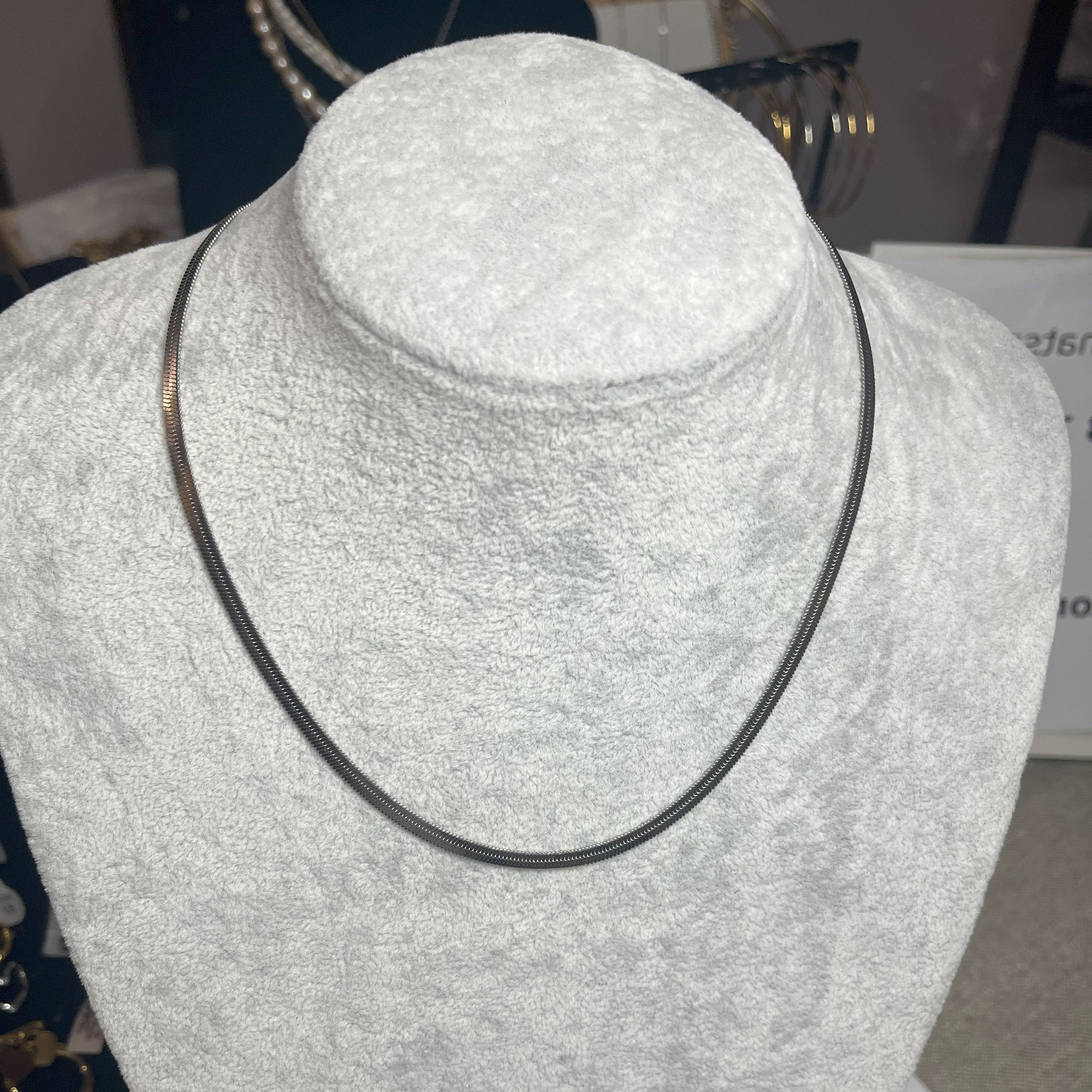 Collana Snake in acciaio premium in placcatura argento, con design ultra-sottile fluido, esposta su busto grigio chiaro