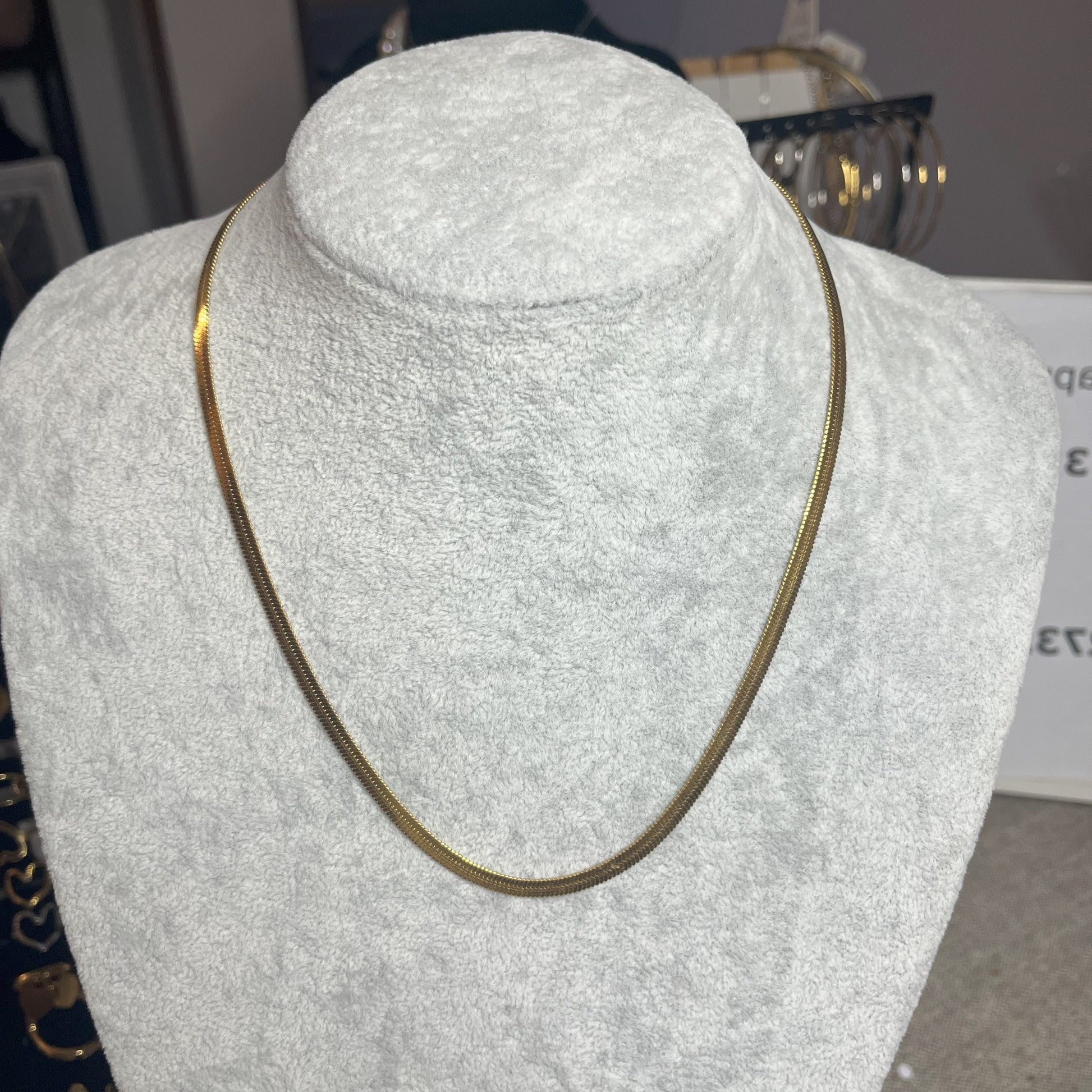 Collana Snake in acciaio premium in placcatura oro, con design ultra-sottile fluido, esposta su busto grigio chiaro
