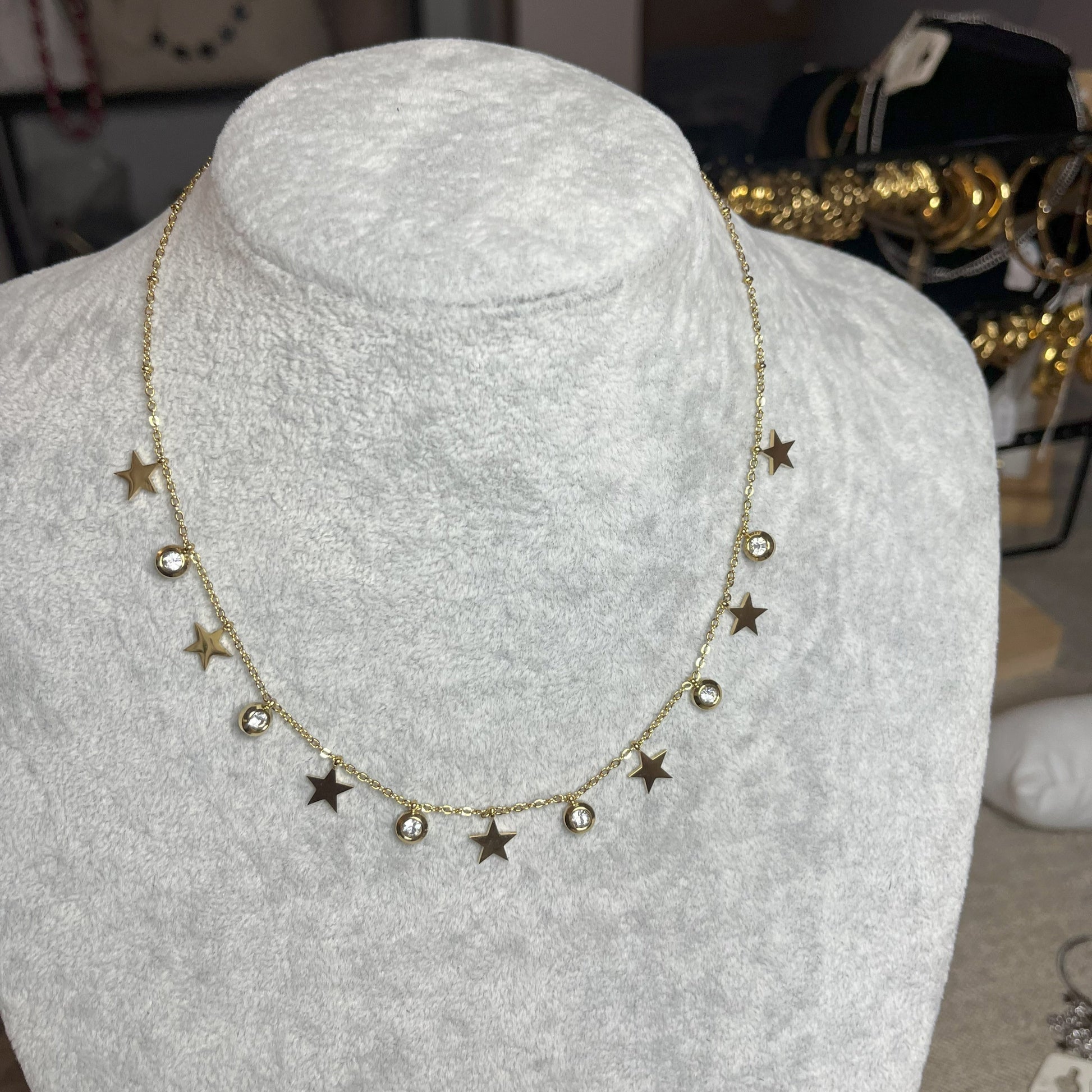 Collana Stellar Dreams in acciaio placcato oro con stelle dorate alternate a punti luce scintillanti su catena delicata, esposta su busto grigio