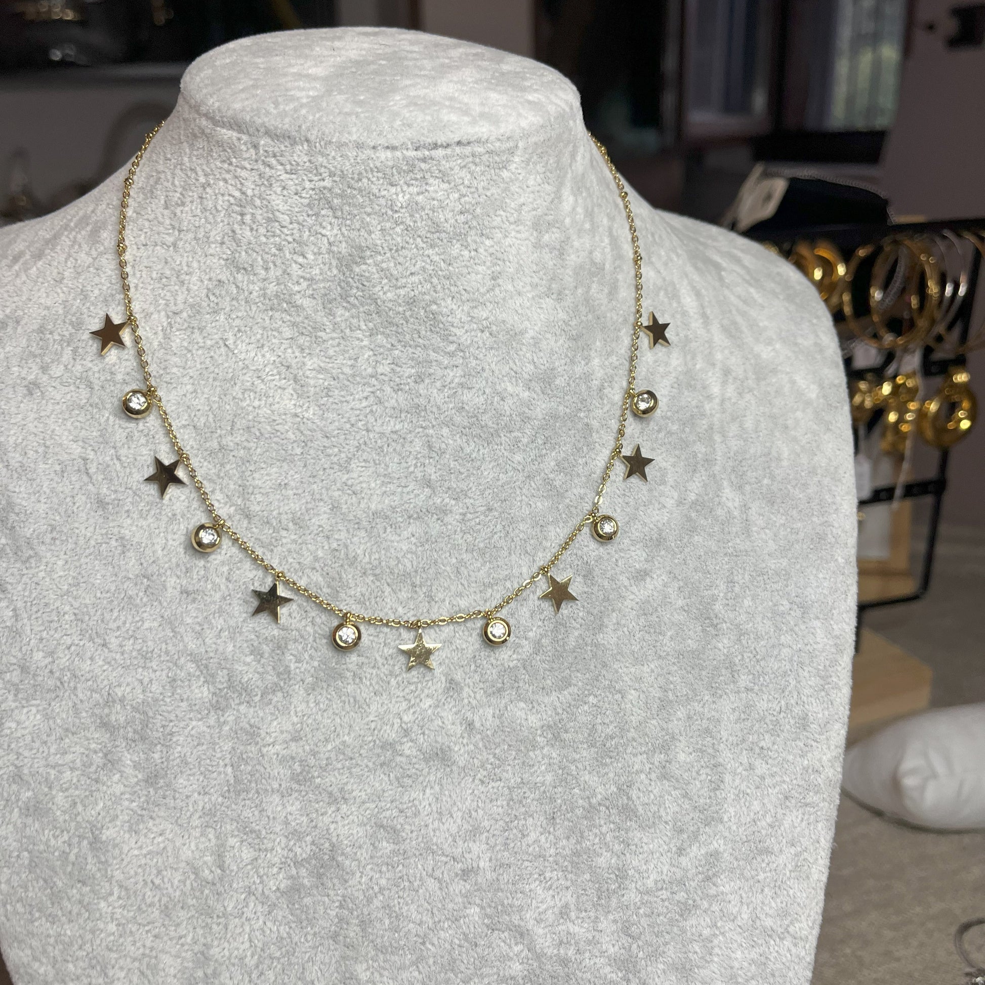 Collana Stellar Dreams in acciaio placcato oro con stelle dorate alternate a punti luce scintillanti su catena delicata, esposta su busto grigio