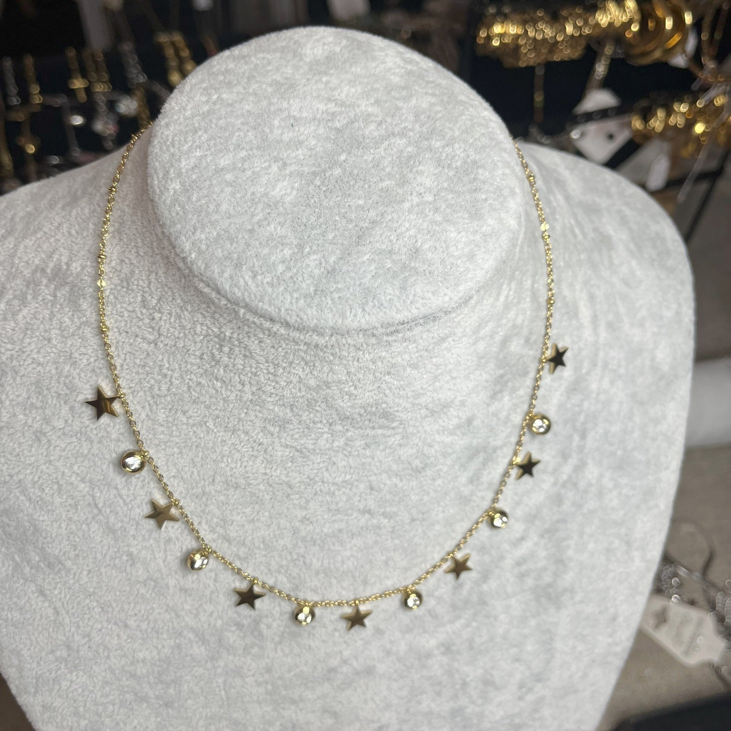 Collana Stellar Dreams in acciaio placcato oro con stelle dorate alternate a punti luce scintillanti su catena delicata, esposta su busto grigio