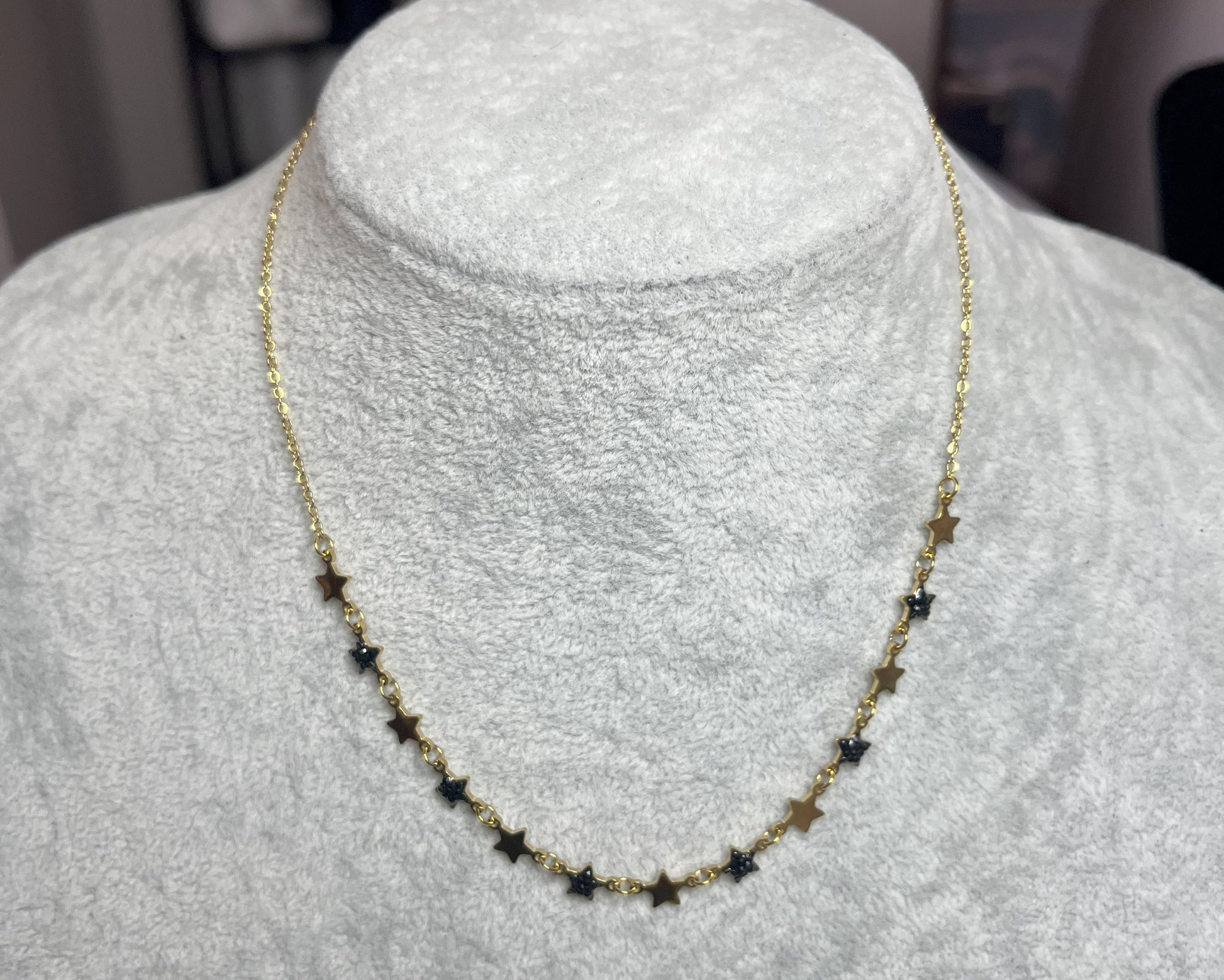 Collana Stelline Dorate - elegante catena dorata con piccole stelle nere alternate, gioiello minimalista su busto espositore