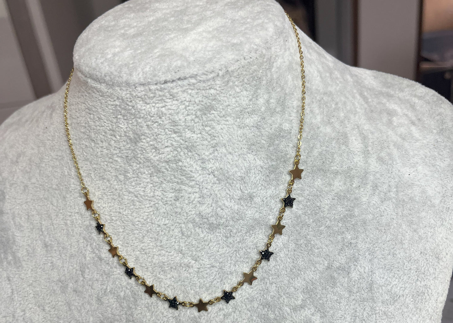 Collana Stelline Dorate - elegante catena dorata con piccole stelle nere alternate, gioiello minimalista su busto espositore