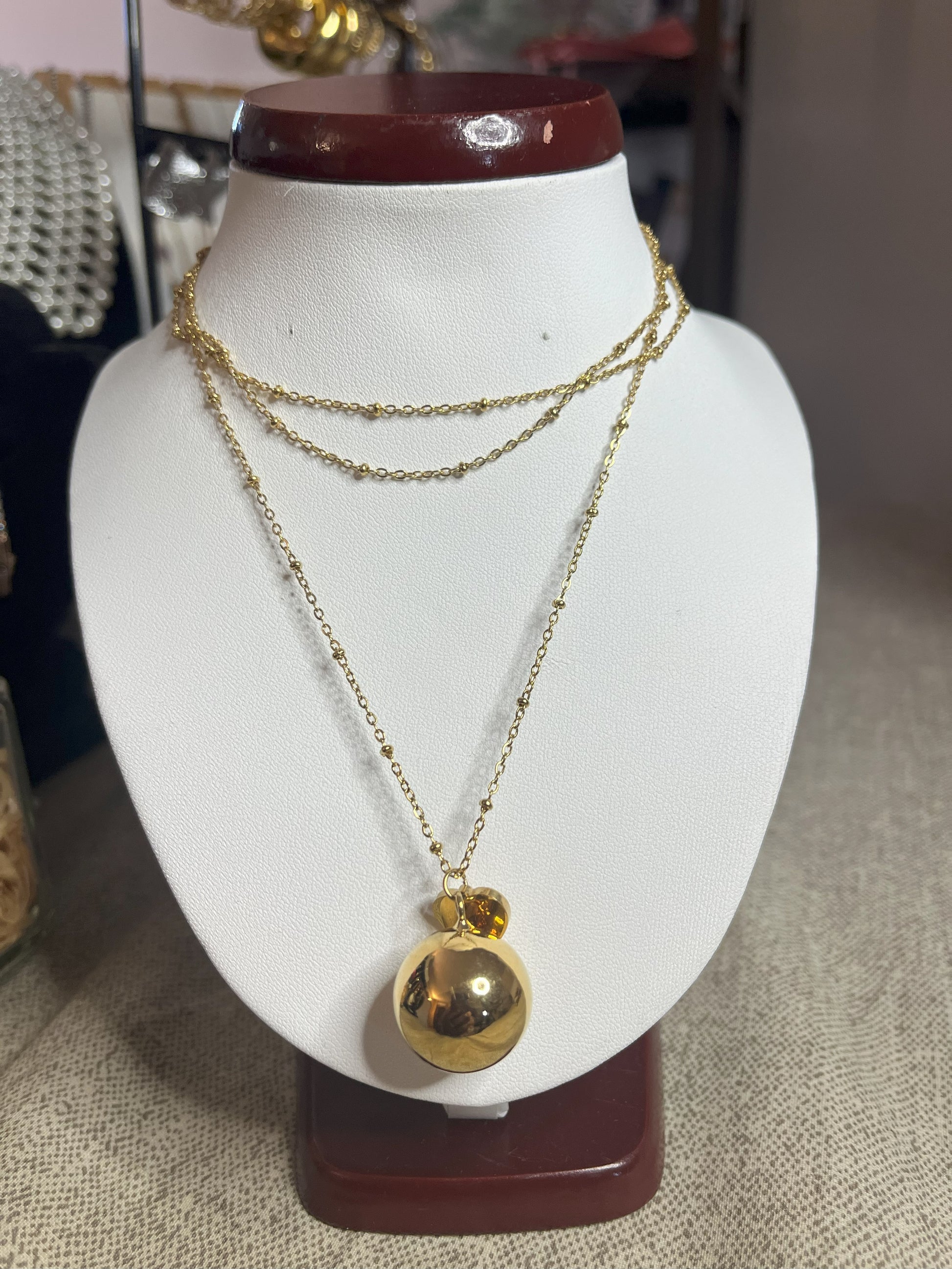 Collana Doppio Giro con sfera a sonaglio e ciondolo cuore in acciaio premium, disponibile nelle variante placcato oro, esposta su busto espositore bianco