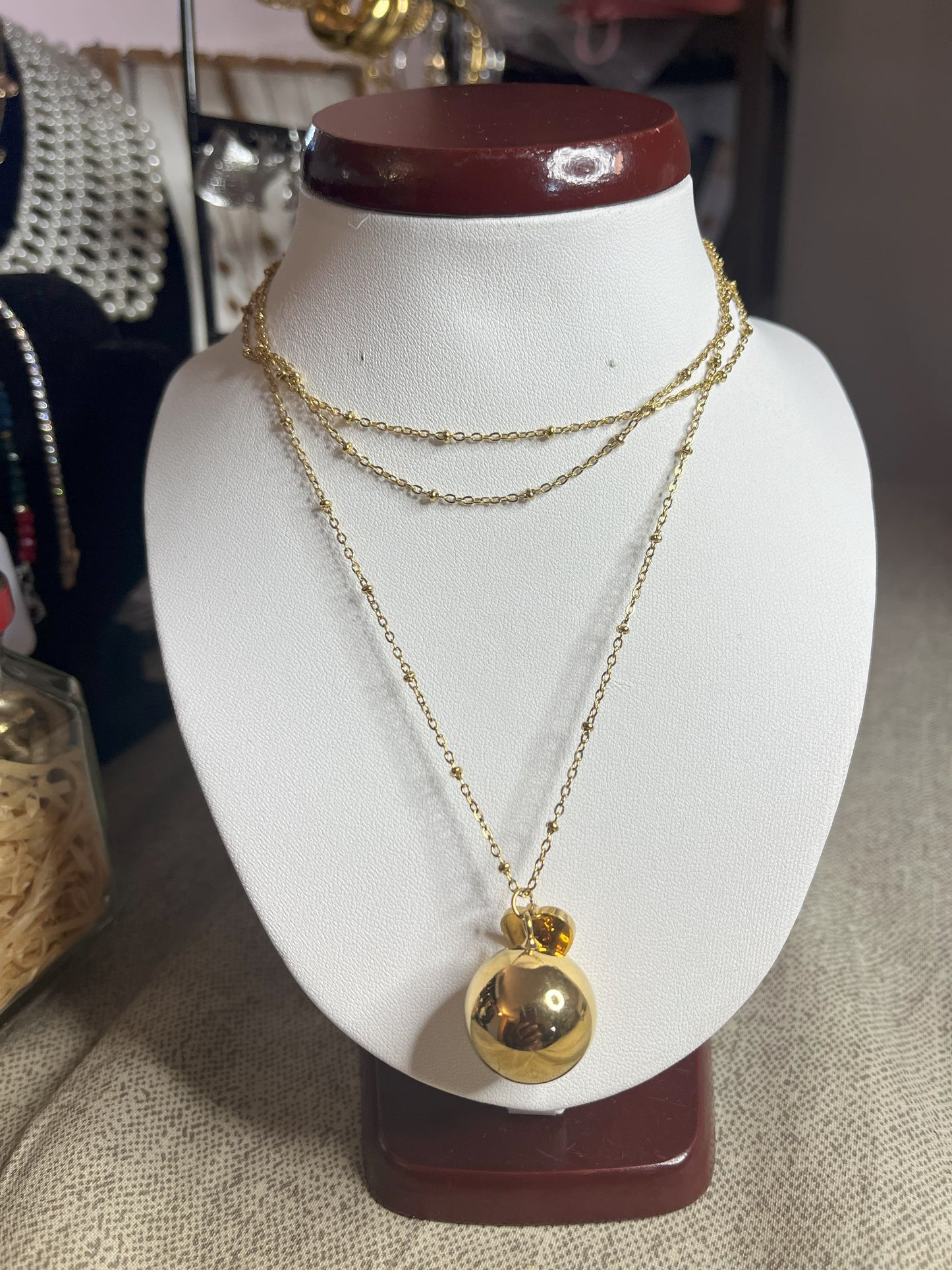 Collana Doppio Giro con sfera a sonaglio e ciondolo cuore in acciaio premium, disponibile nelle variante placcato oro, esposta su busto espositore bianco