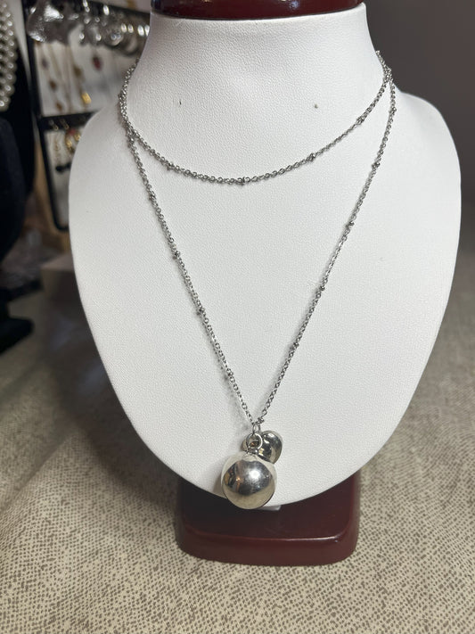 Collana Doppio Giro con sfera a sonaglio e ciondolo cuore in acciaio premium, disponibile nelle variante placcato argento, esposta su busto espositore bianco