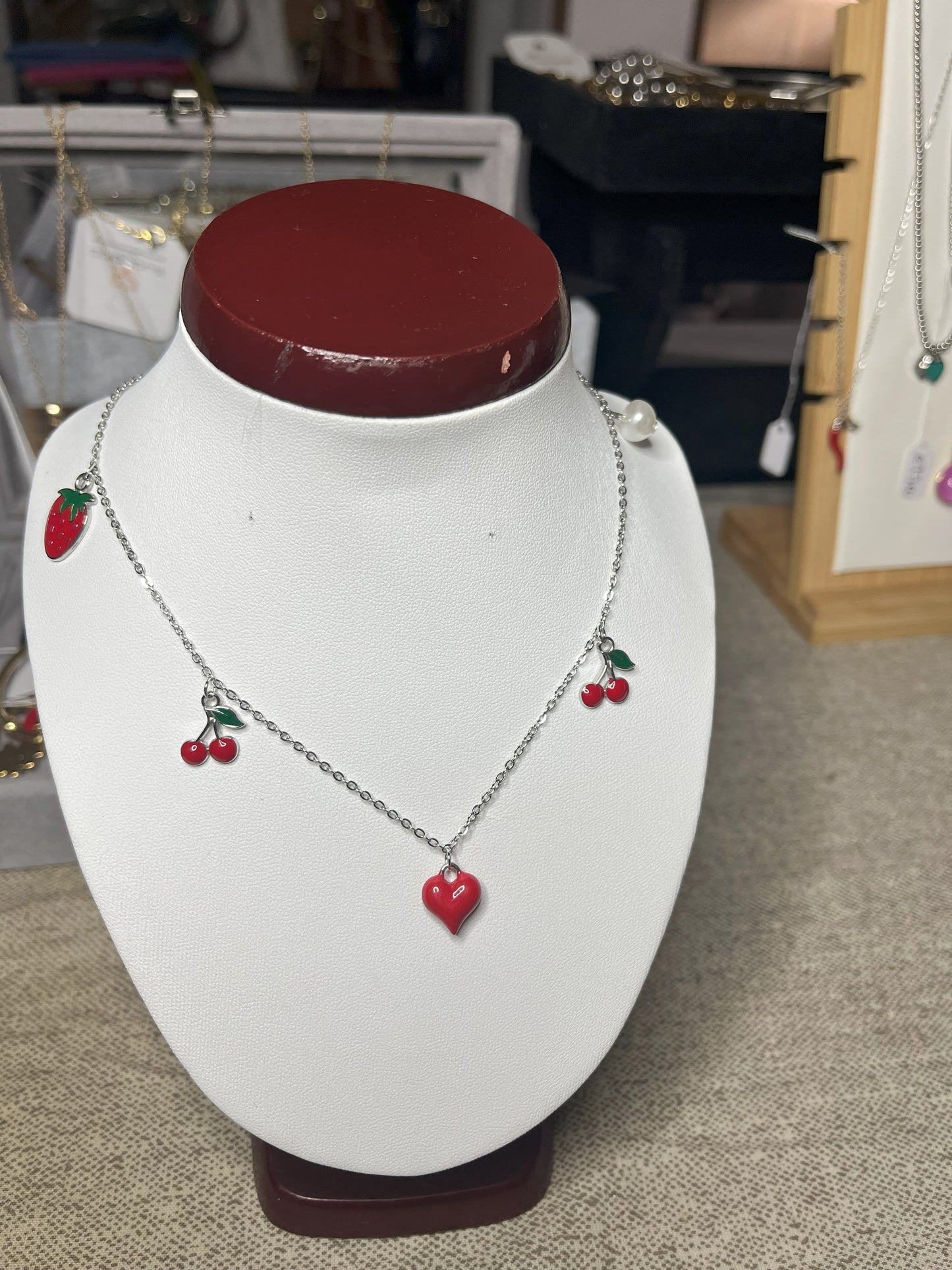 Collana Good Vibes con catena argentata e ciondoli colorati a forma di cuore, ciliegie e fragola, esposta su busto porta gioielli bianco