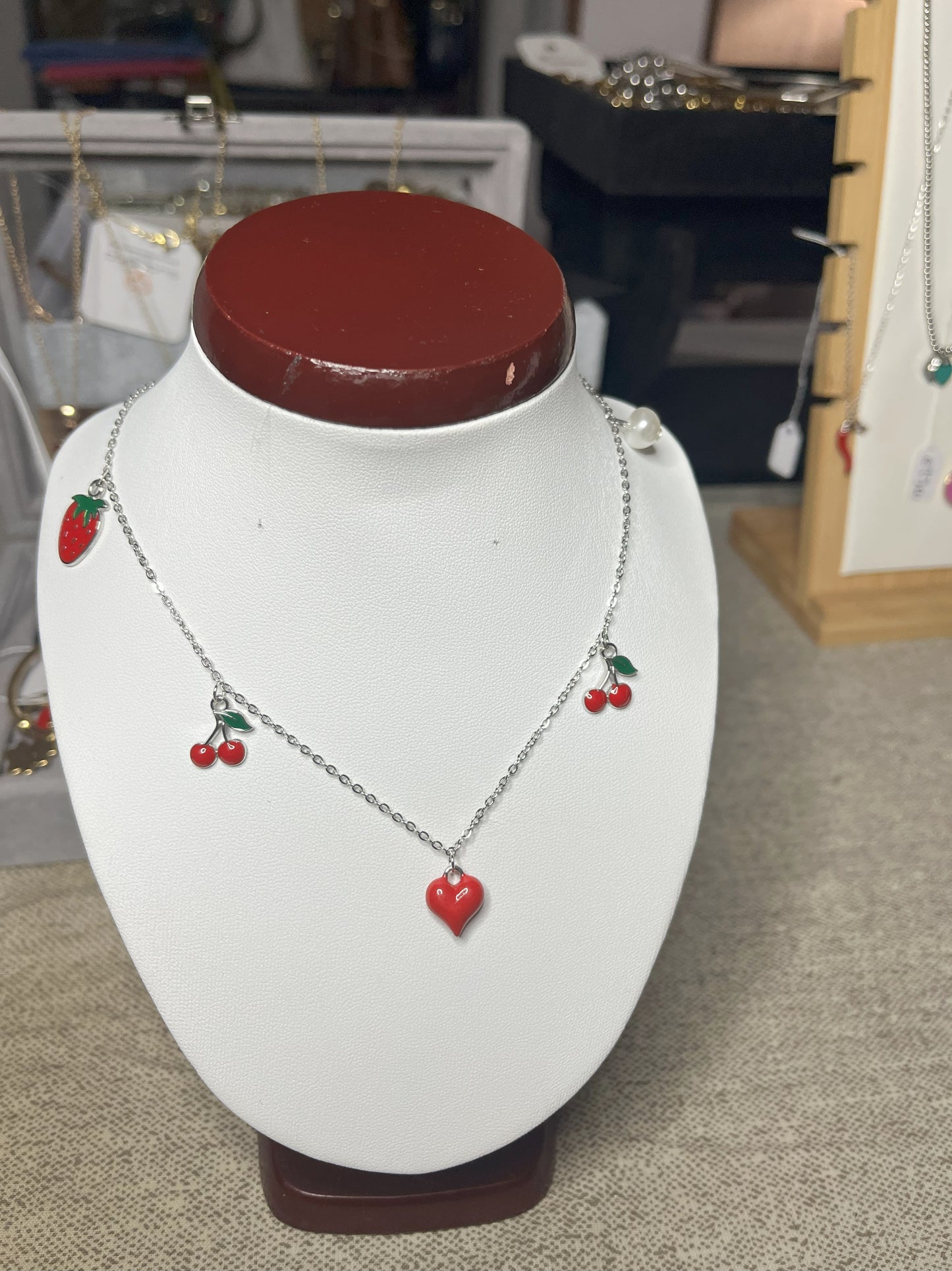 Collana Good Vibes con catena argentata e ciondoli colorati a forma di cuore, ciliegie e fragola, esposta su busto porta gioielli bianco