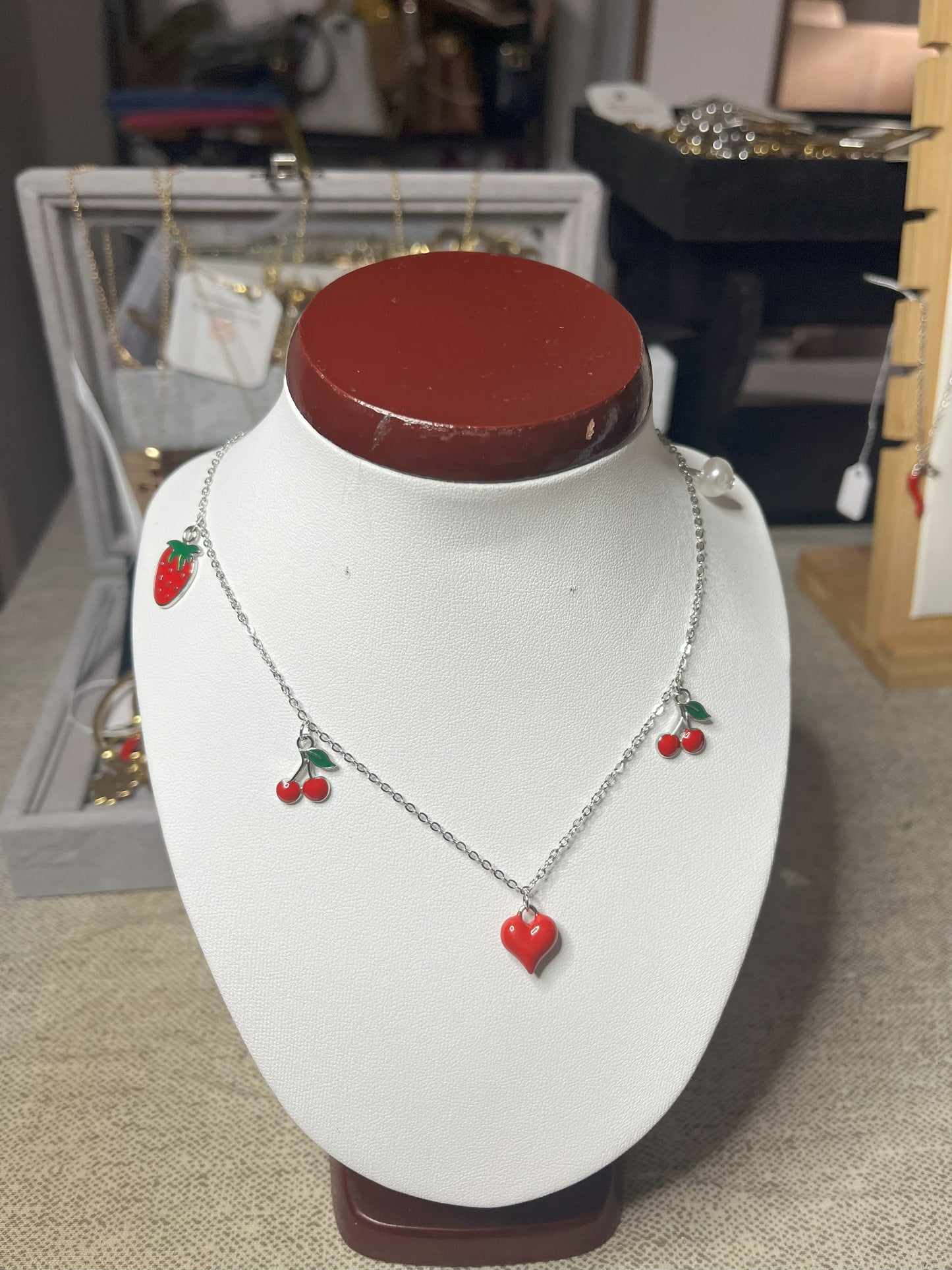 Collana Good Vibes con catena argentata e ciondoli colorati a forma di cuore, ciliegie e fragola, esposta su busto porta gioielli bianco