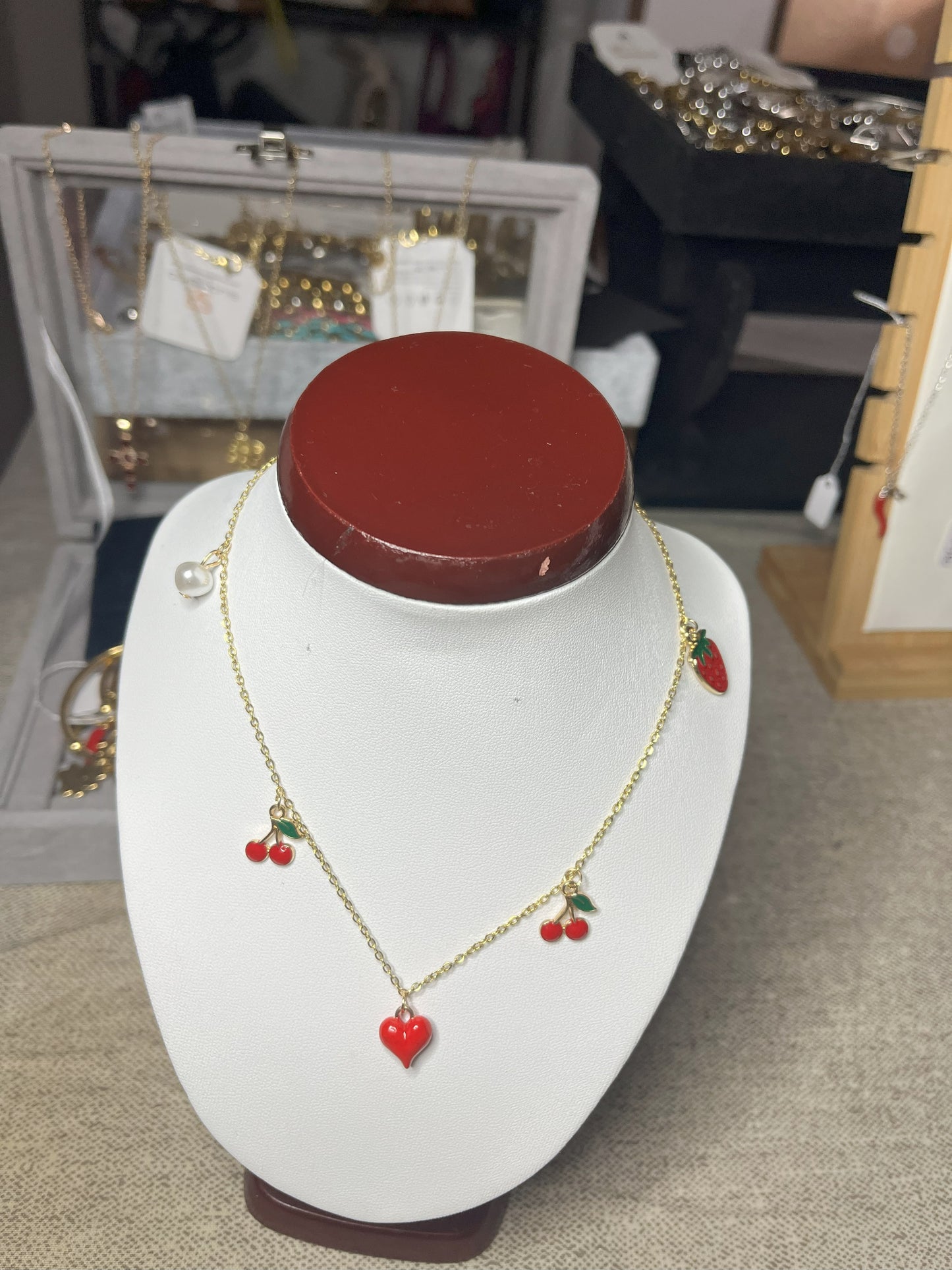 Collana Good Vibes con catena argentata e ciondoli colorati a forma di cuore, ciliegie e fragola, esposta su busto porta gioielli bianco