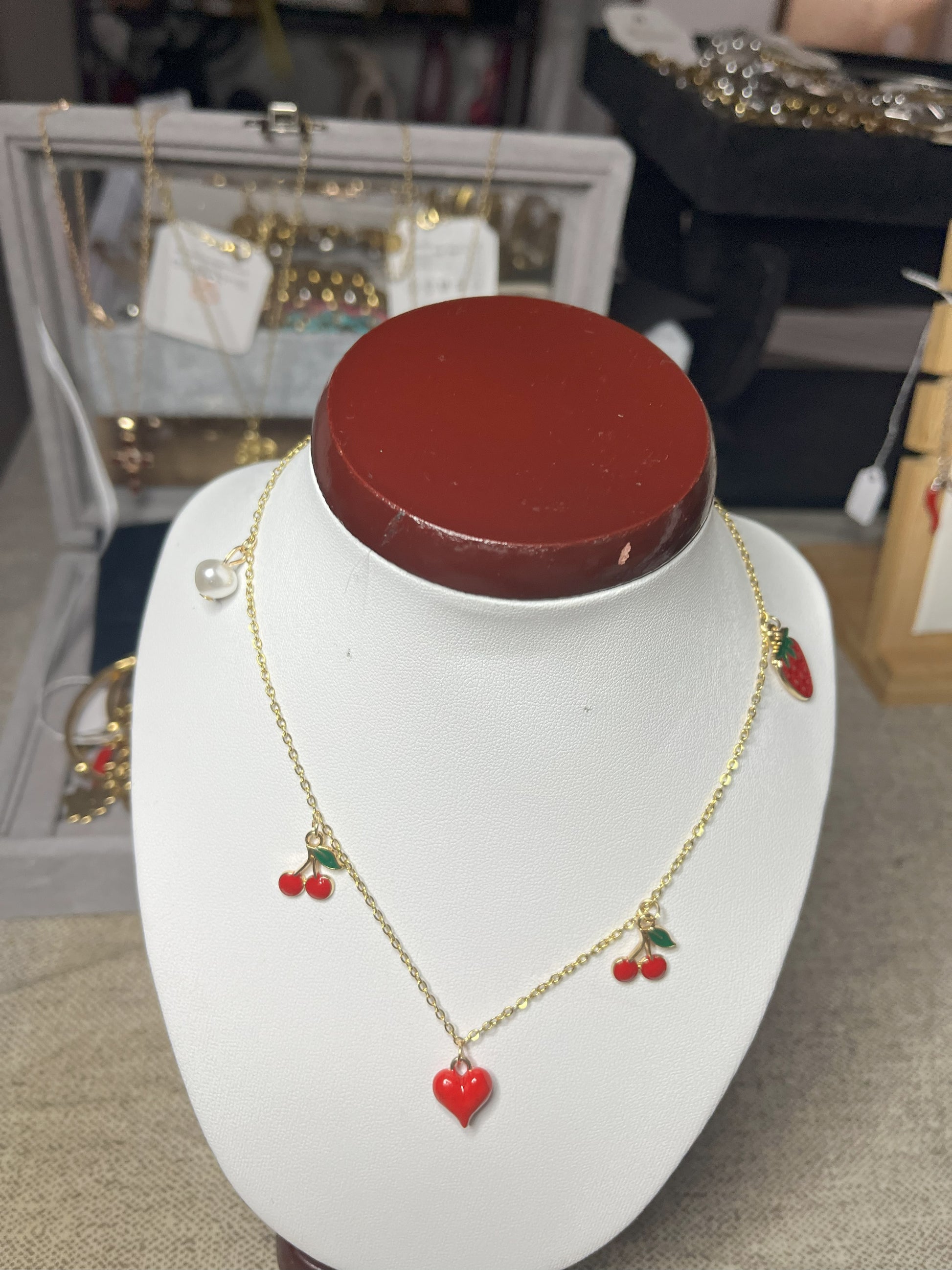 Collana Good Vibes con catena argentata e ciondoli colorati a forma di cuore, ciliegie e fragola, esposta su busto porta gioielli bianco