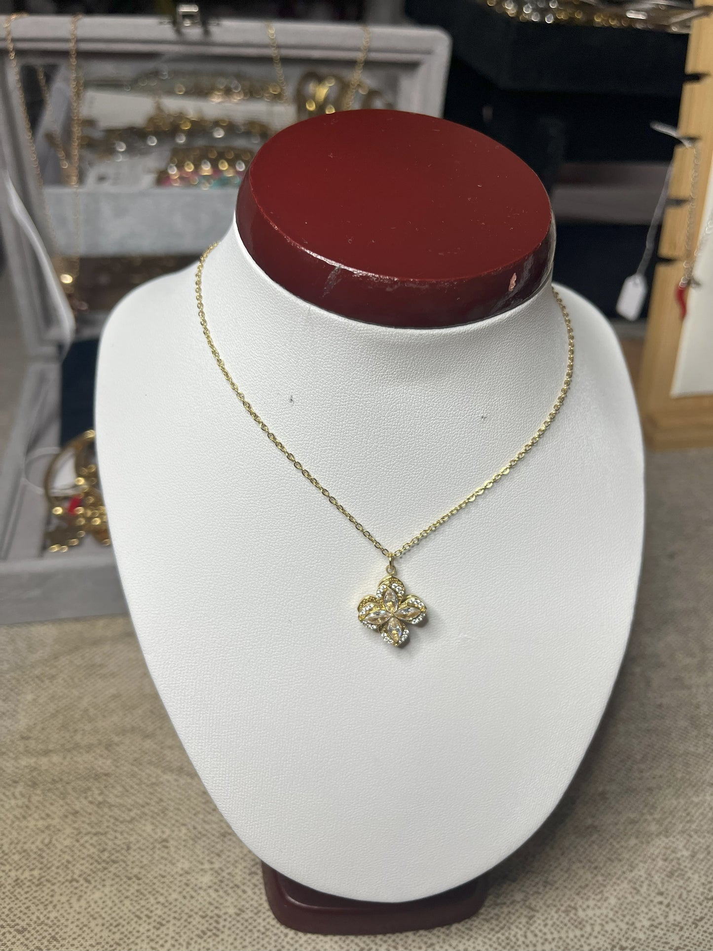 Collana in acciaio con ciondolo quadrifoglio decorato con zirconi su busto espositore bianco con base rossa