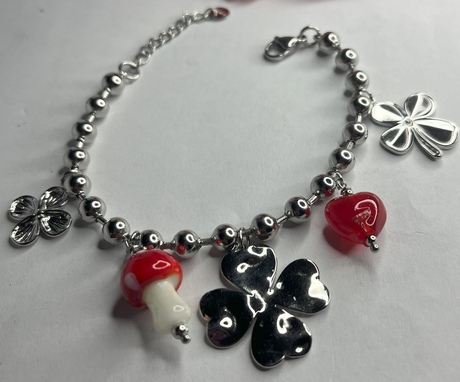 Braccialetto Giardino Magico in acciaio inox argentato con charms floreali, cuori rossi e perline colorate su sfondo grigio