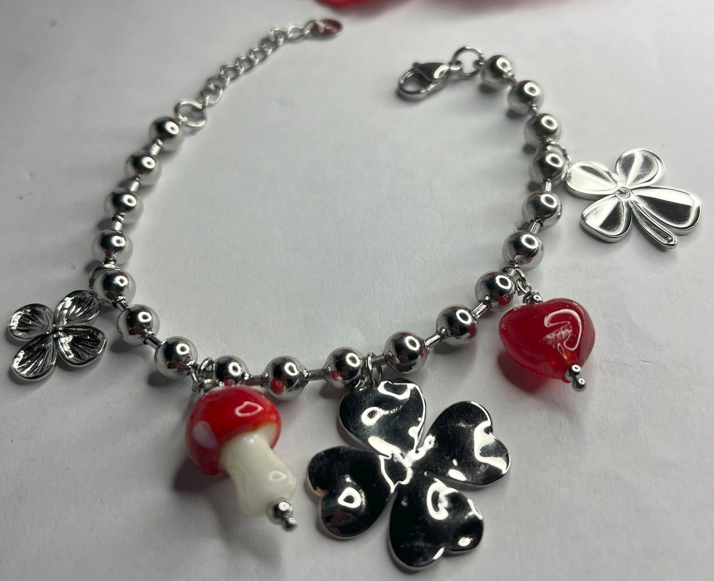 Braccialetto Giardino Magico in acciaio inox argentato con charms floreali, cuori rossi e perline colorate su sfondo grigio