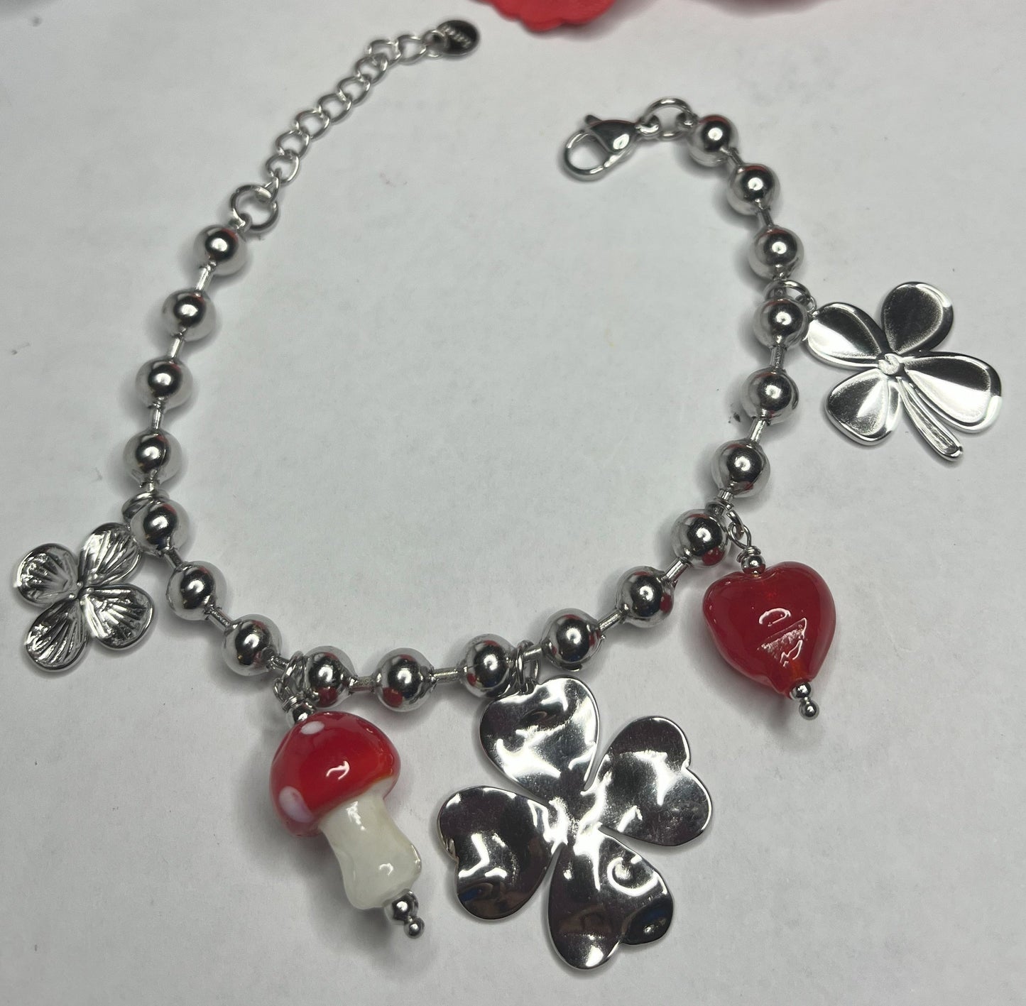 Braccialetto Giardino Magico in acciaio inox argentato con charms floreali, cuori rossi e perline colorate su sfondo grigio