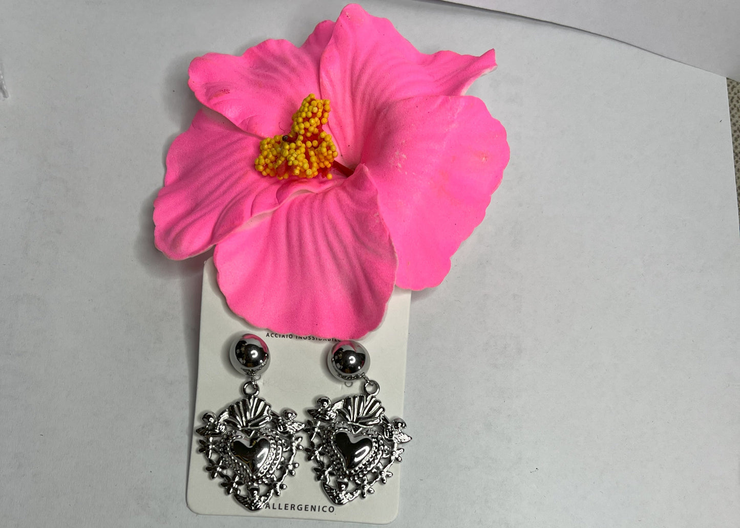 Orecchini dorati a forma di sacro cuore con dettagli intarsiati e lavorazione artigianale su sfondo con fiore rosa