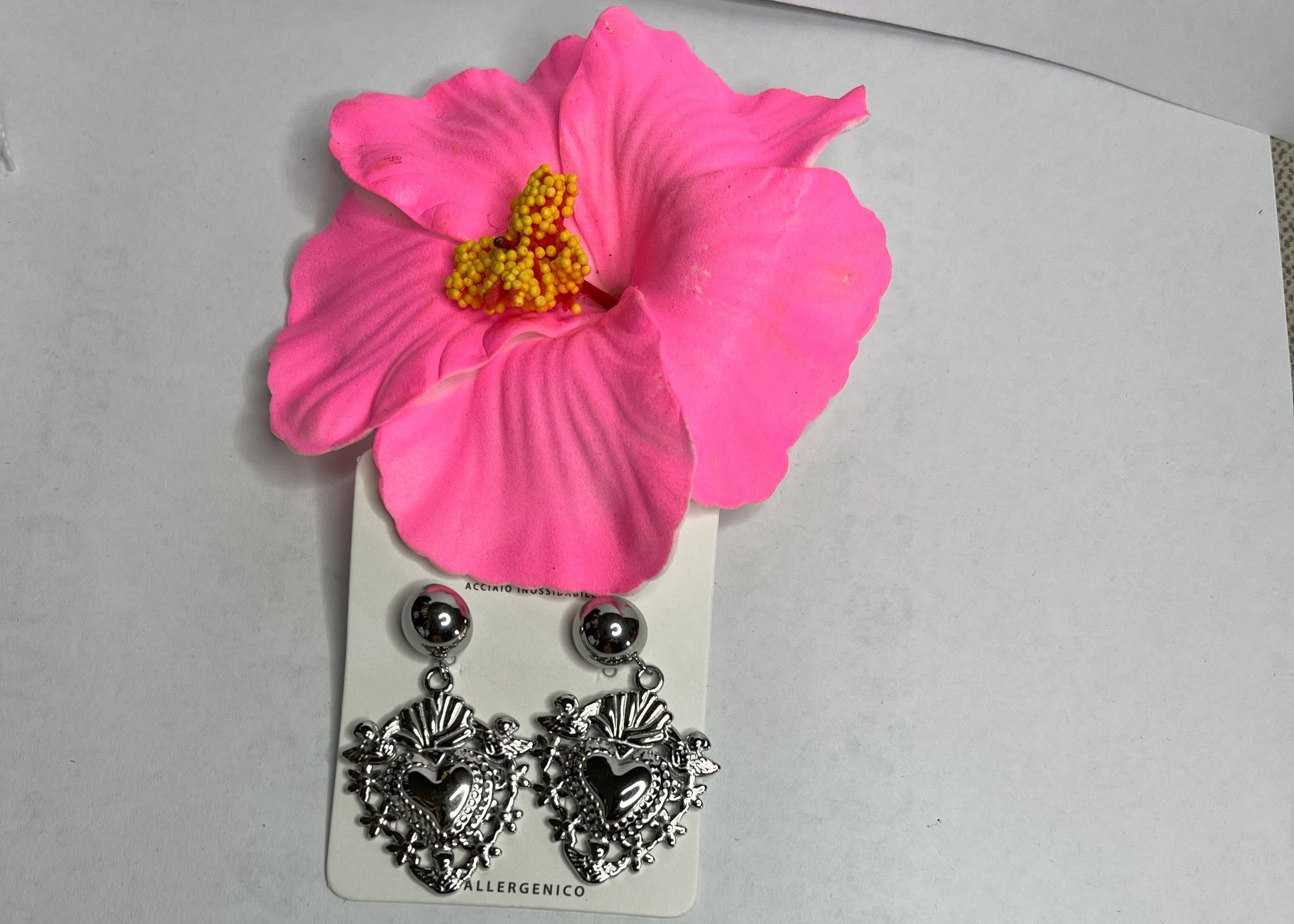 Orecchini dorati a forma di sacro cuore con dettagli intarsiati e lavorazione artigianale su sfondo con fiore rosa