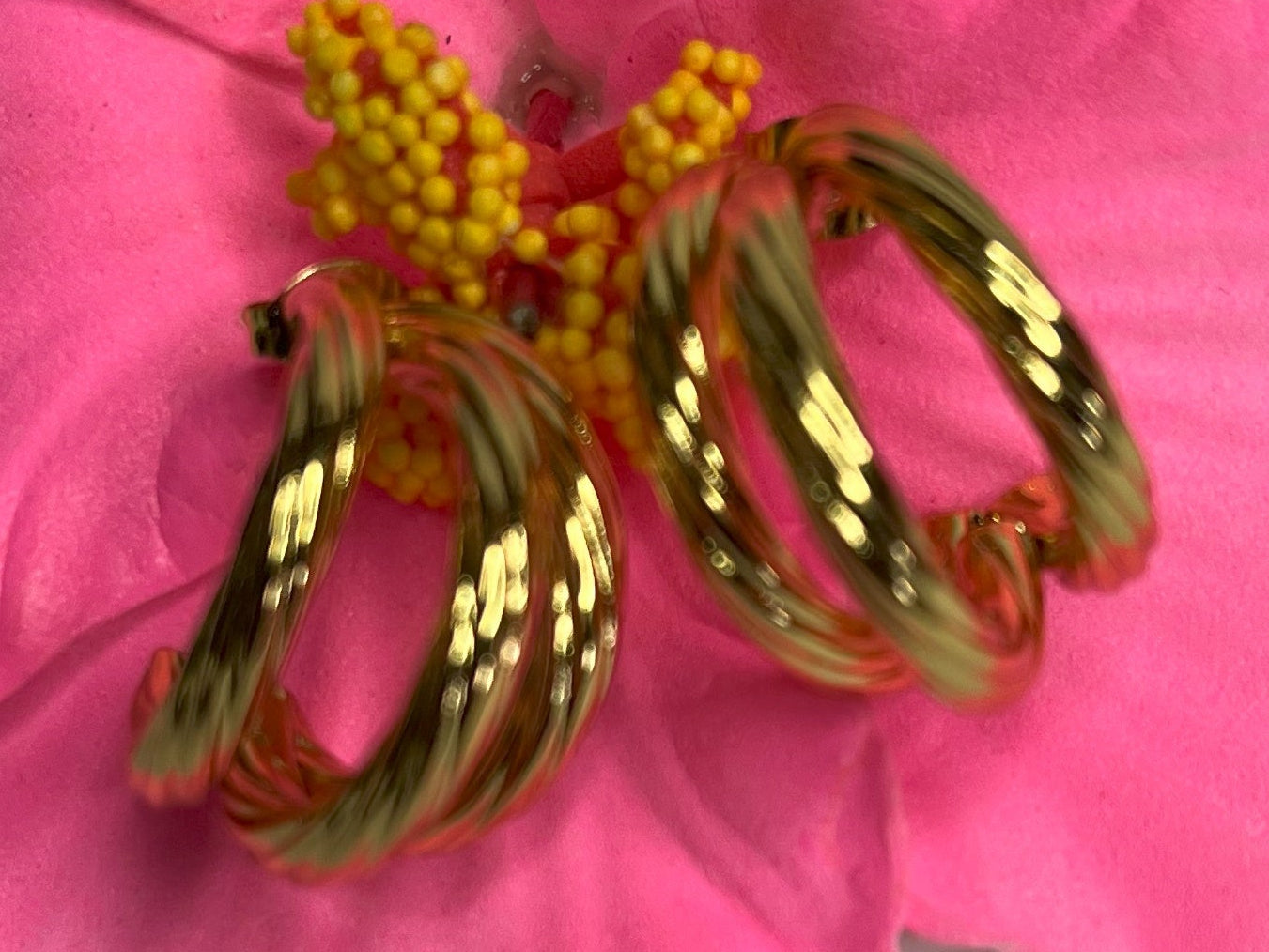 Orecchini Helix placcati oro premium con design a spirale tridimensionale, fotografati su petali di fiore rosa fucsia