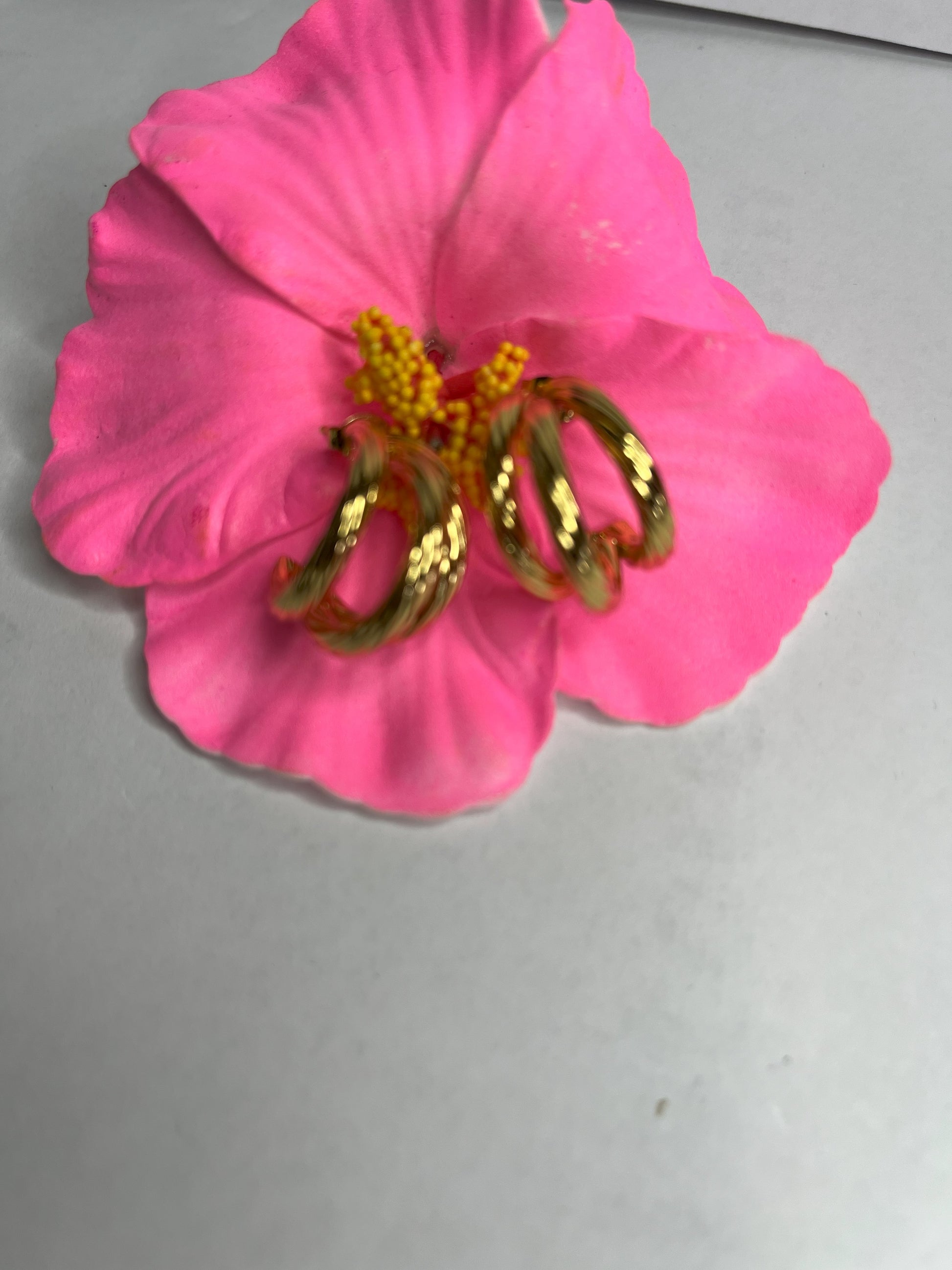 Orecchini Helix placcati oro premium con design a spirale tridimensionale, fotografati su petali di fiore rosa fucsia