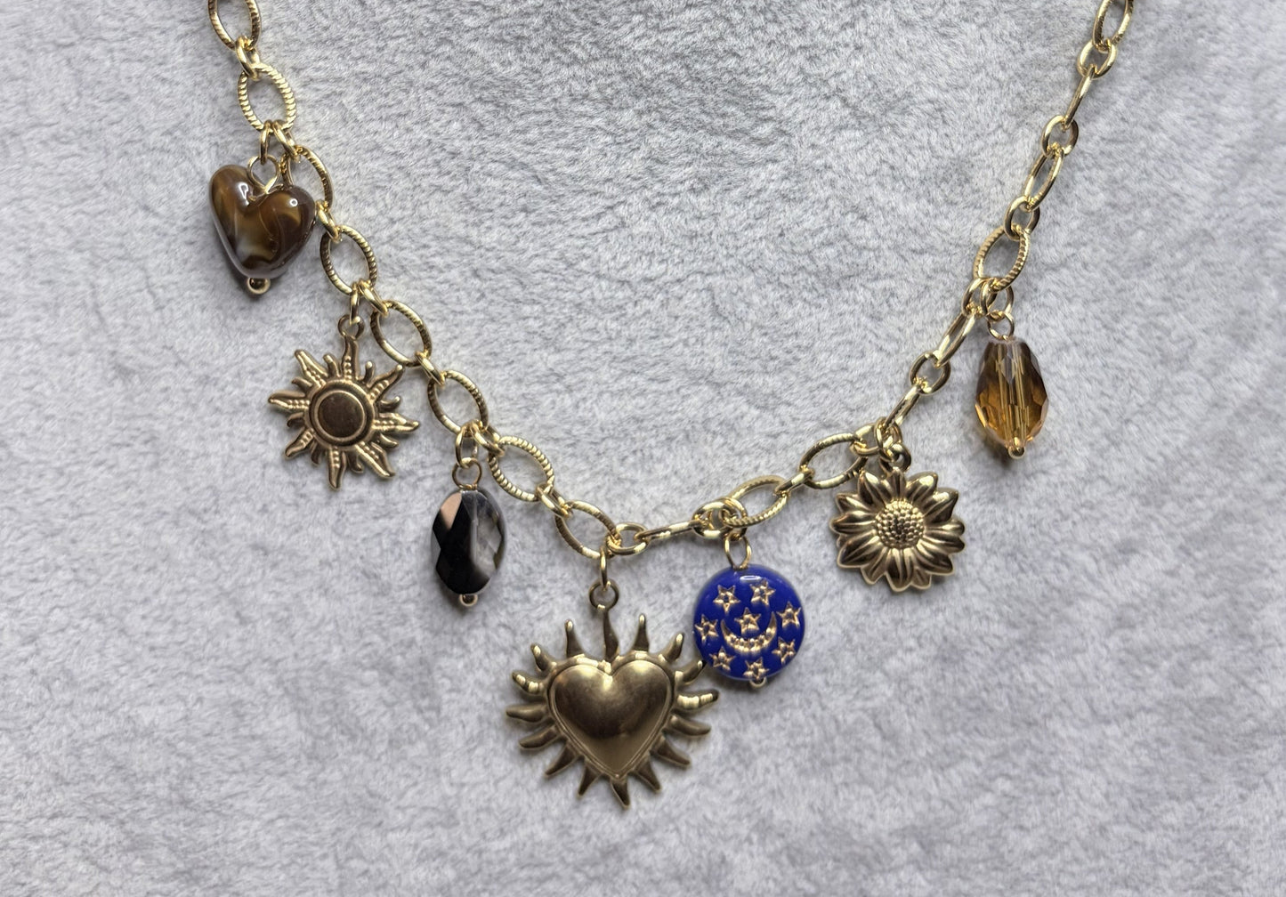 Dettaglio charm collana dorata: sacro cuore raggiante, perla blu stellata e cristallo nero