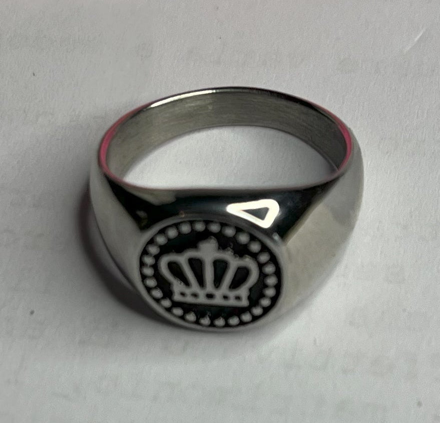 Anello Mignolo Regina in acciaio premium con design regale inciso, variante placcato argento, fotografato su superficie bianca con fiore rosa
