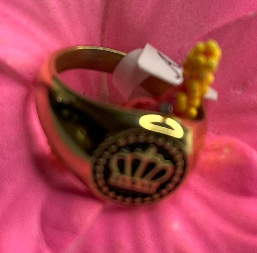 Anello Mignolo Regina in acciaio premium con design regale inciso, variante placcato oro, fotografato su superficie bianca con fiore rosa