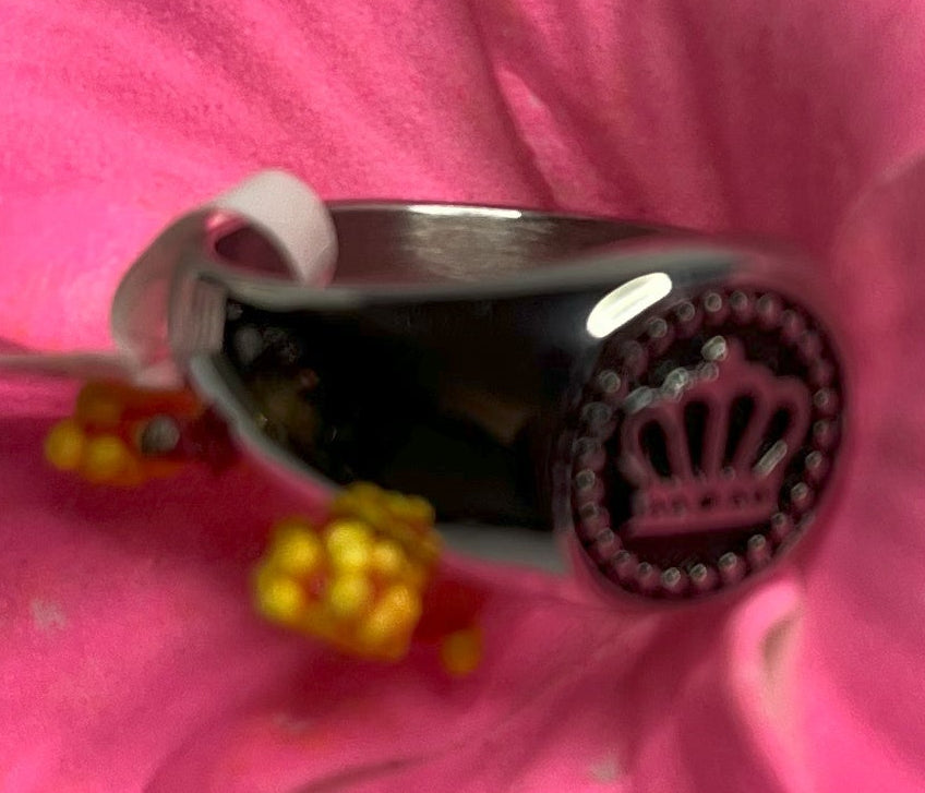 Anello Mignolo Regina in acciaio premium con design regale inciso, variante placcato argento, fotografato su superficie bianca con fiore rosa
