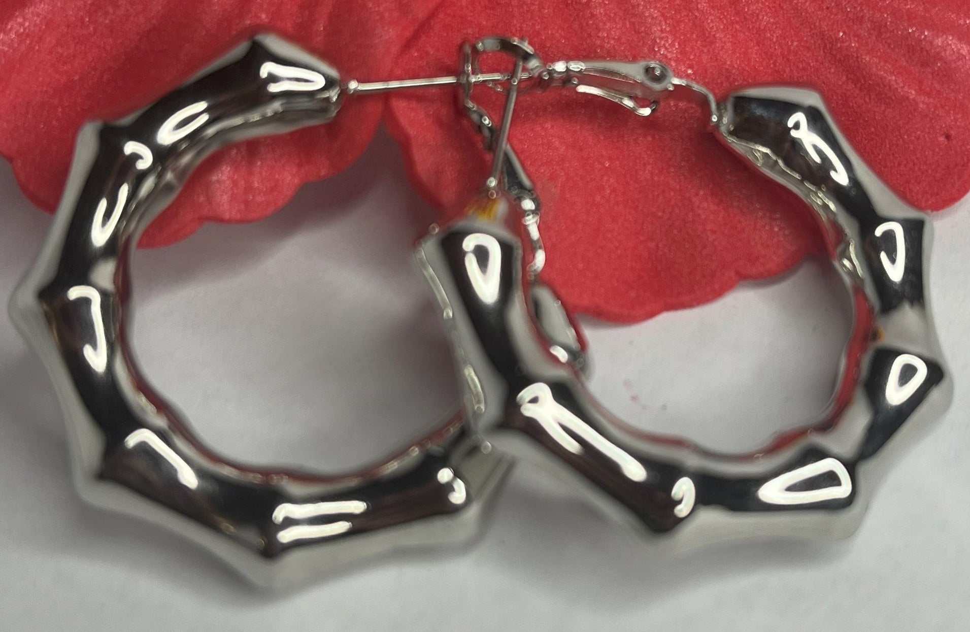 Orecchini Bambù Prezioso placcati argento con texture bambù a cerchio, design naturale elegante su sfondo bianco con fiore rosso decorativo