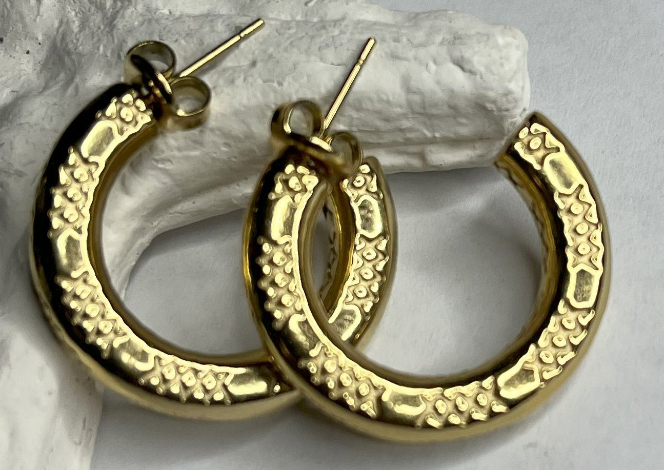 Orecchini a cerchio placcati oro con texture decorativa tridimensionale, appoggiati su corallo bianco