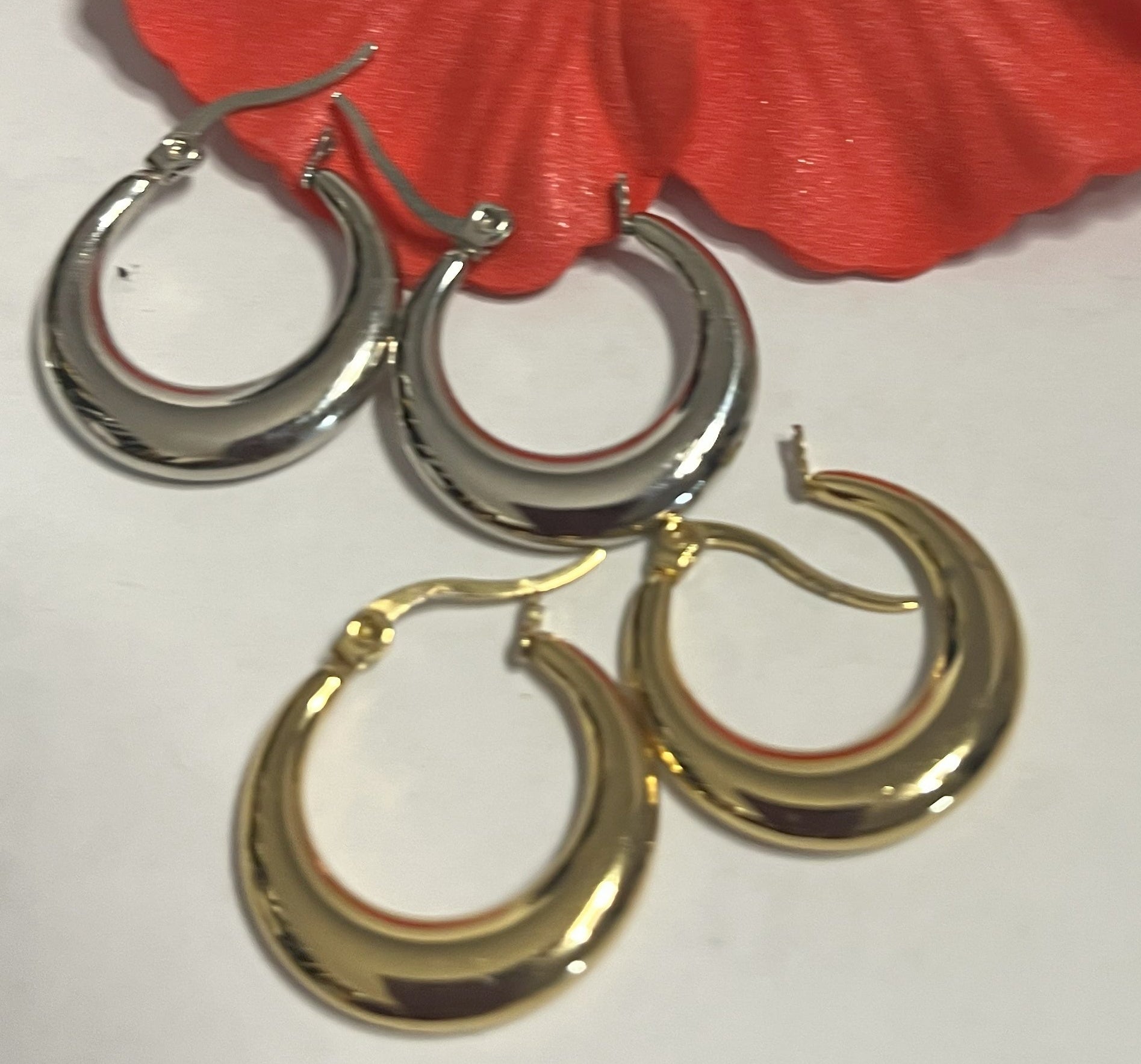 Set di orecchini creoli placcati, due paia in oro e argento, disposti su sfondo neutro con fiore rosso decorativo