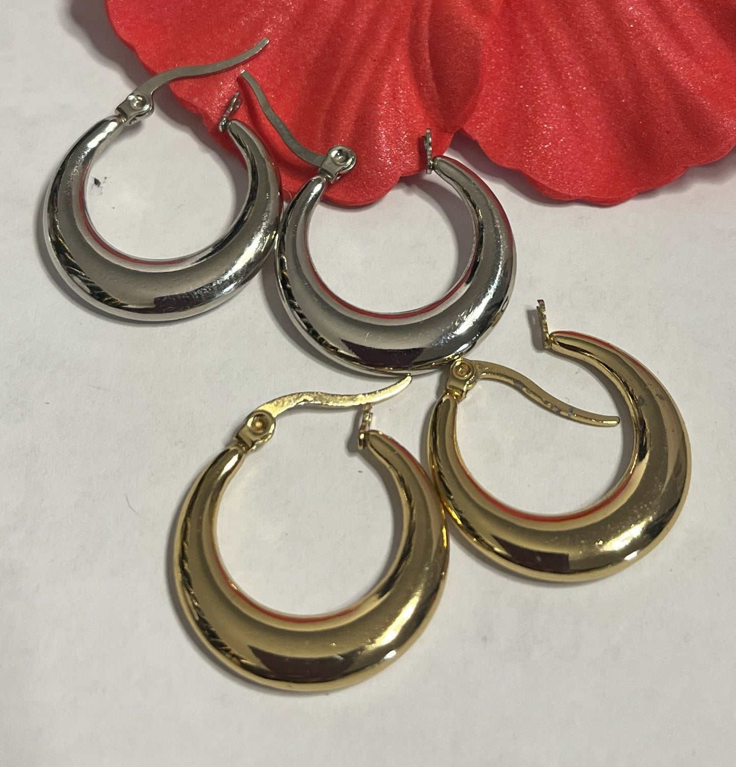 Set di orecchini creoli placcati, due paia in oro e argento, disposti su sfondo neutro con fiore rosso decorativo