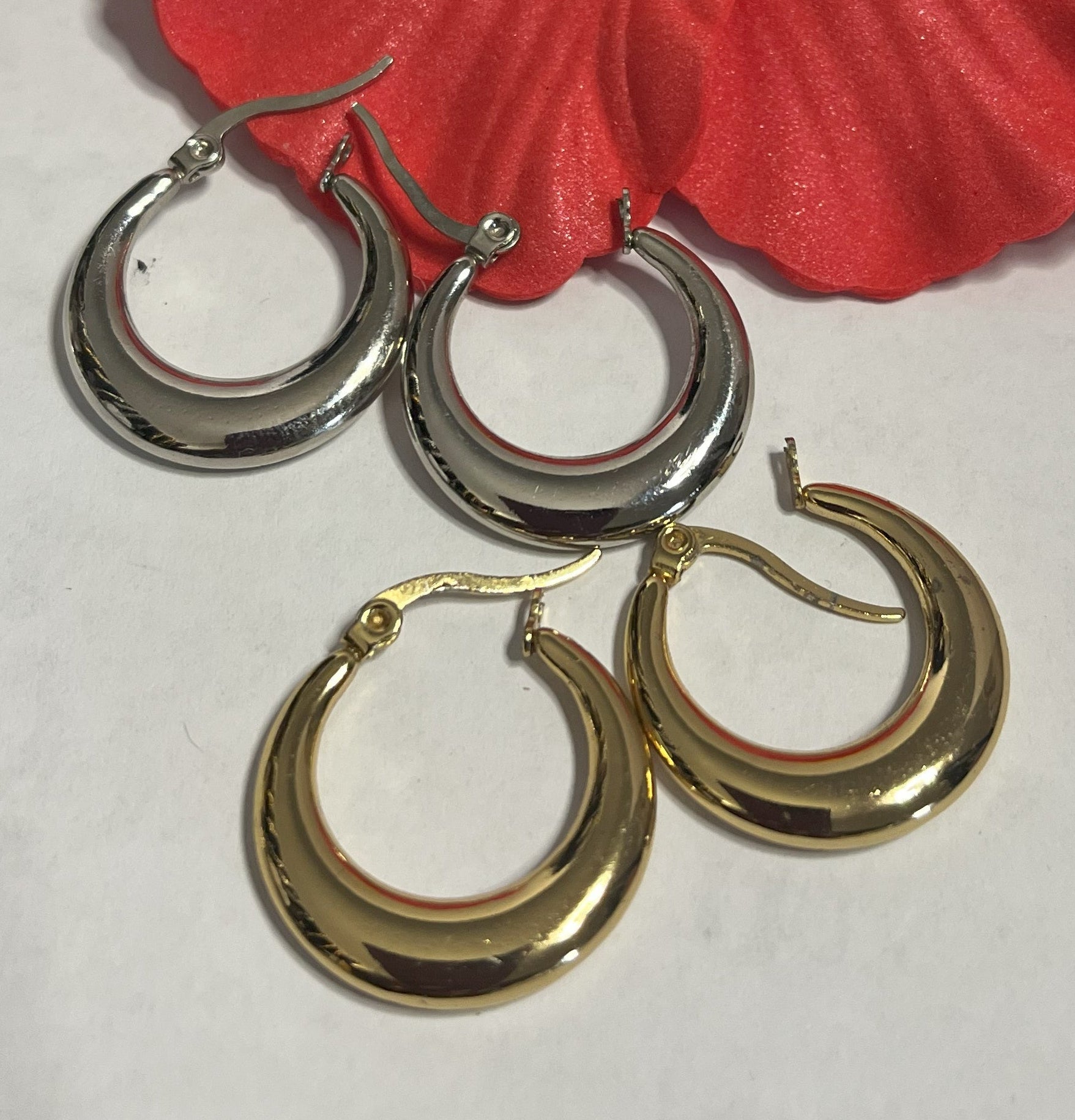 Set di orecchini creoli placcati, due paia in oro e argento, disposti su sfondo neutro con fiore rosso decorativo