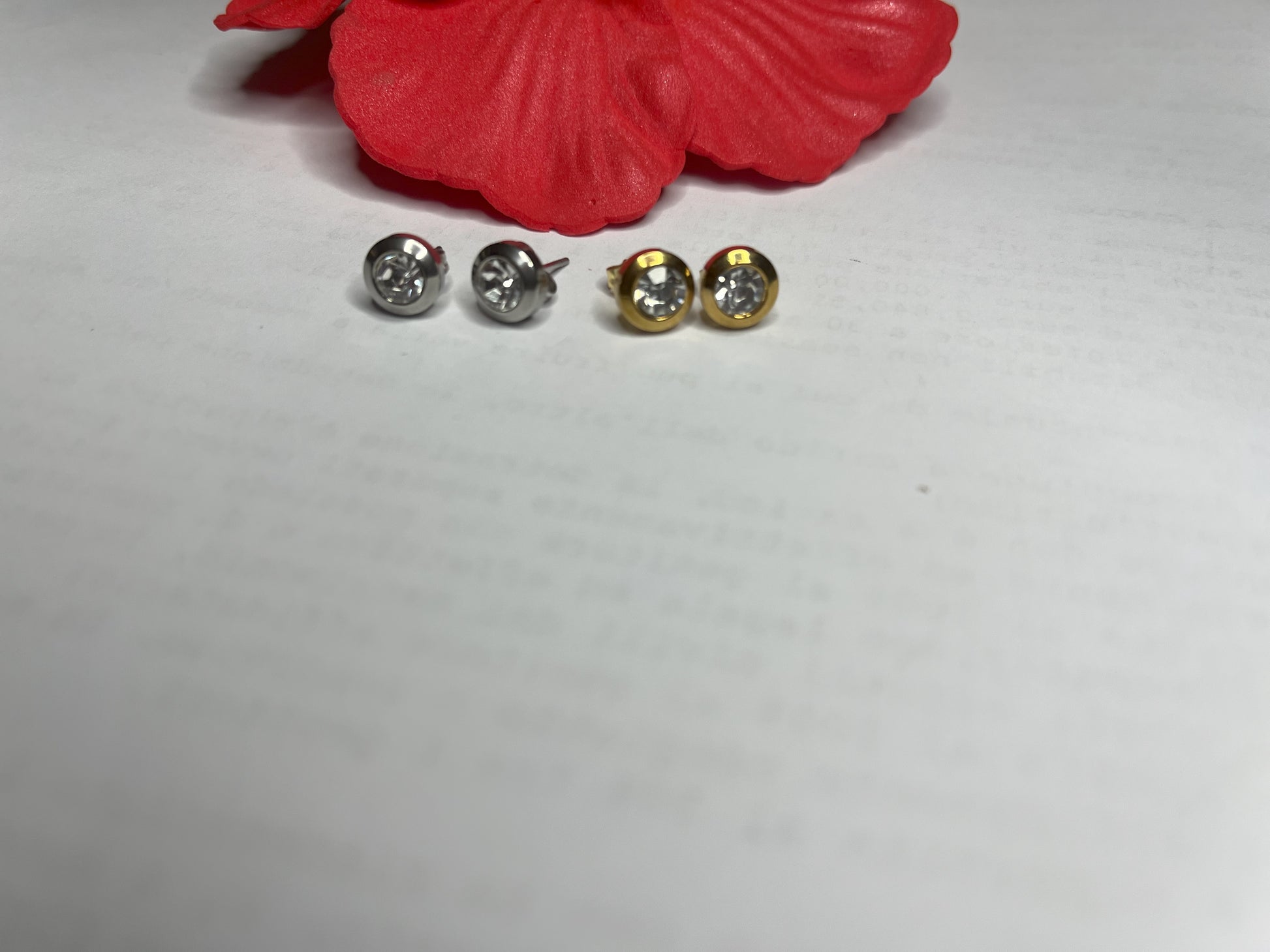 Coppia di orecchini punto luce in acciaio placcato su sfondo bianco con fiore rosso decorativo, design elegante a bottone con chiusura a farfallina