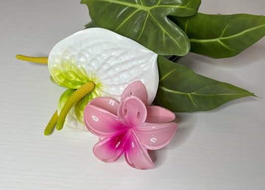 Elegante pinza hawaiana per capelli a forma di fiore con petali lucidi, posizionata accanto a un bouquet di fiori freschi gialli e bianchi
