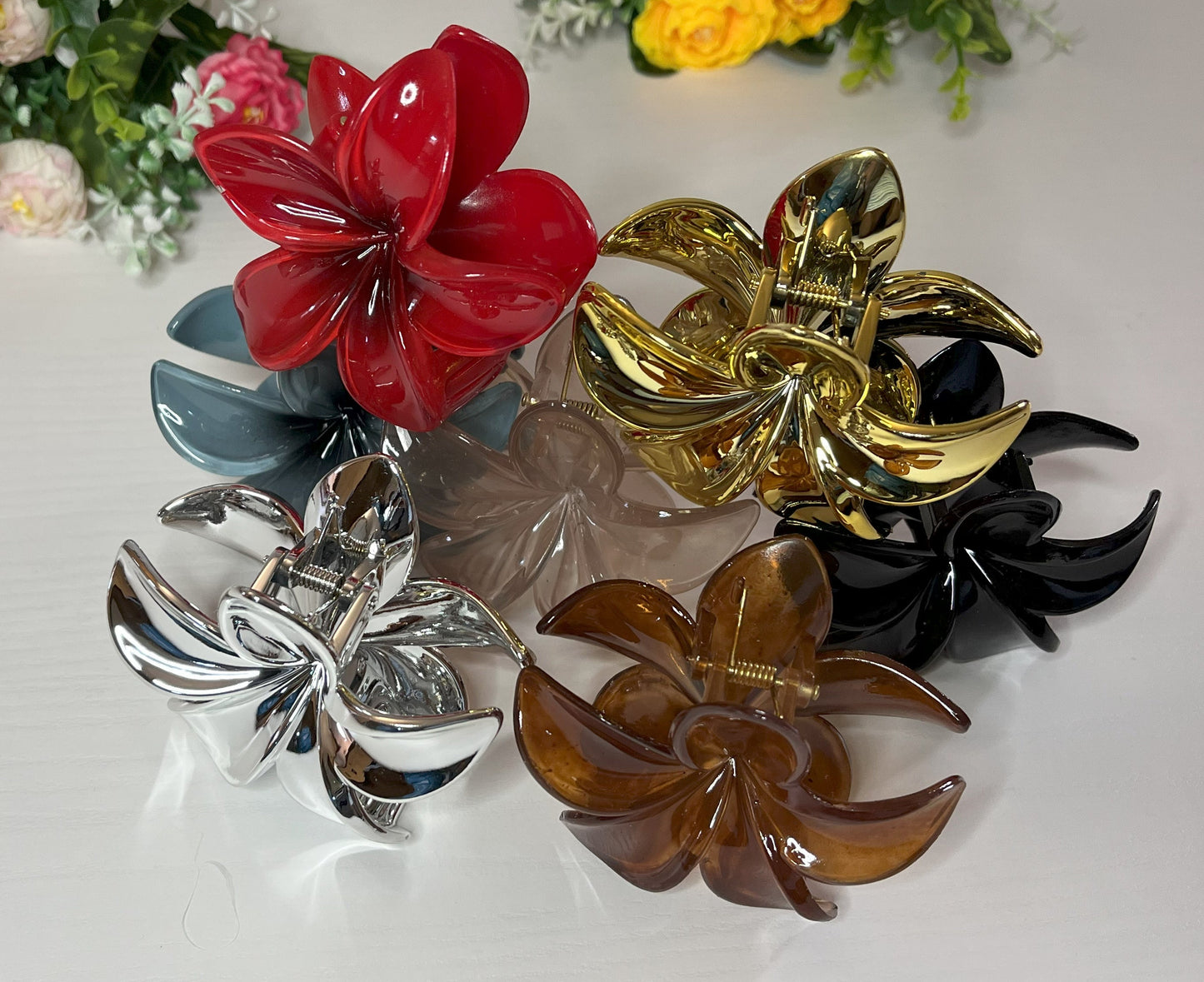 Elegante pinza hawaiana per capelli a forma di fiore con petali lucidi, posizionata accanto a un bouquet di fiori freschi gialli e bianchi