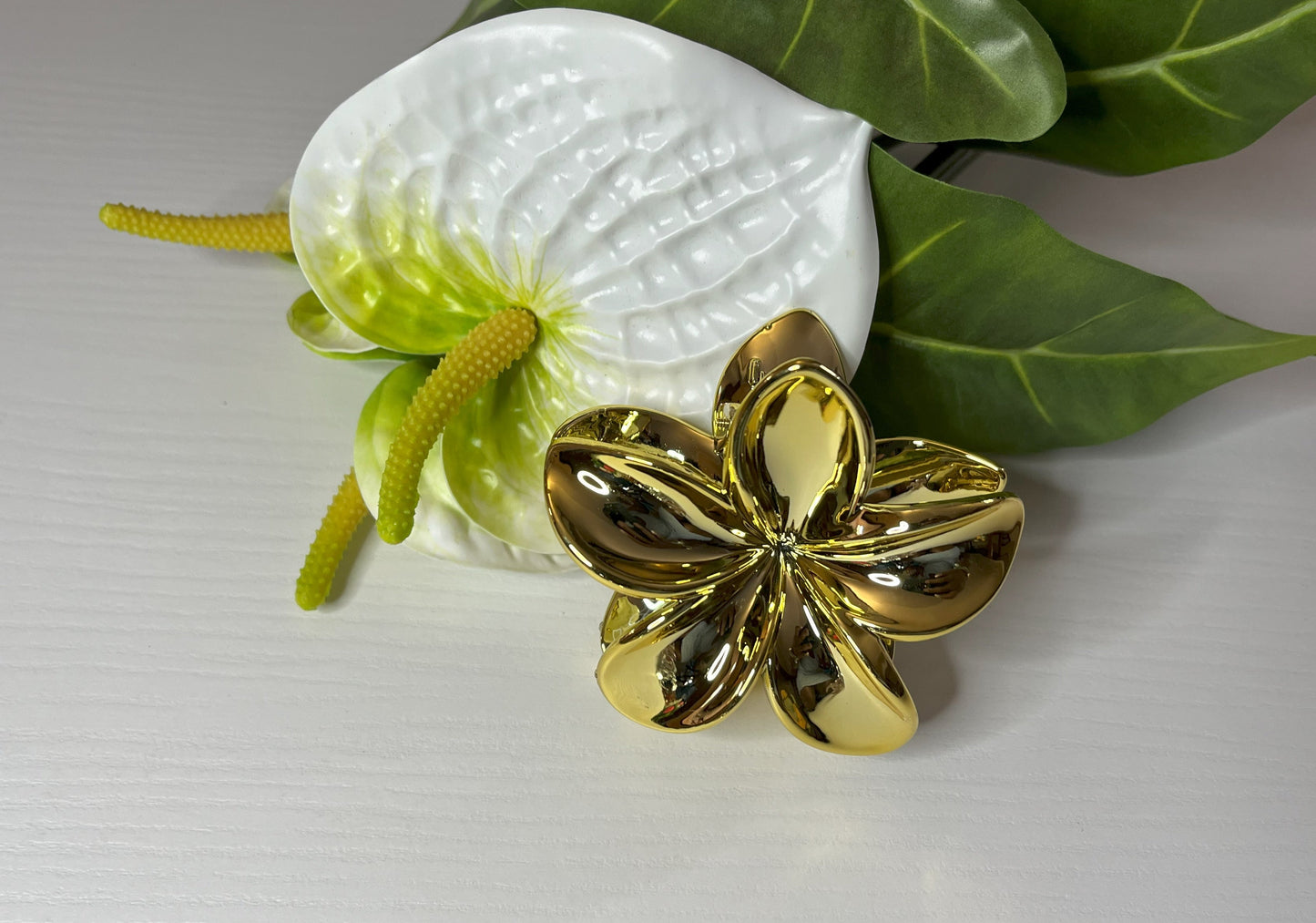 Elegante pinza hawaiana per capelli a forma di fiore con petali lucidi, posizionata accanto a un bouquet di fiori freschi gialli e bianchi
