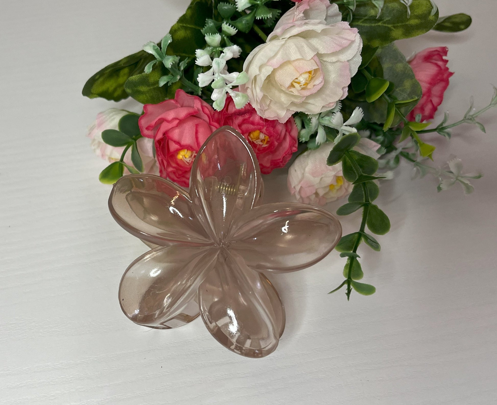 Elegante pinza hawaiana per capelli a forma di fiore con petali lucidi, posizionata accanto a un bouquet di fiori freschi gialli e bianchi