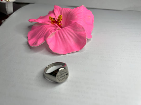 Anello Regina Mamy in acciaio premium placcato argento con incisione dedicata alla maternità, fotografato su superficie bianca con fiore rosa