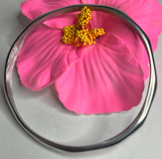 Braccialetto Rinascita in alluminio riciclato fatto a mano, design circolare minimalista con finitura lucida premium, fotografato accanto a un fiore rosa su sfondo neutro
