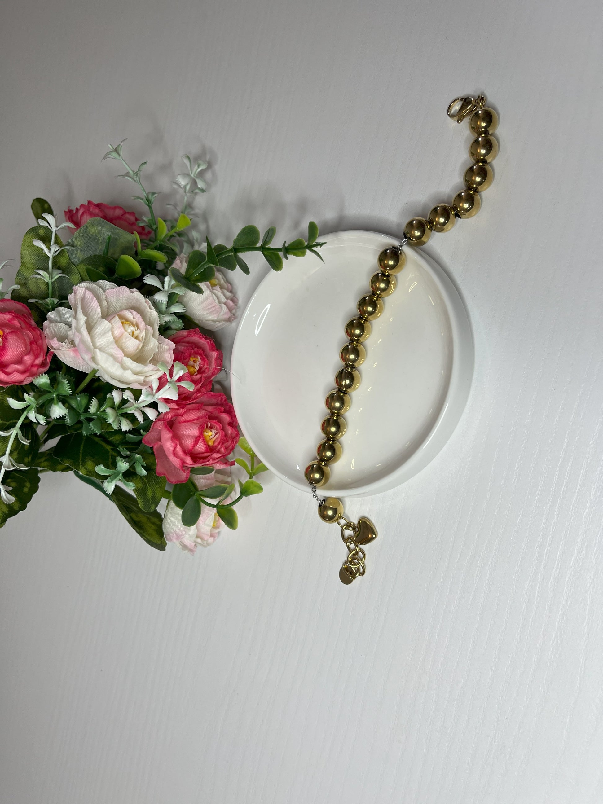Elegante braccialetto con sfere dorate lucide su fiori bianchi rosa e foglie verdi