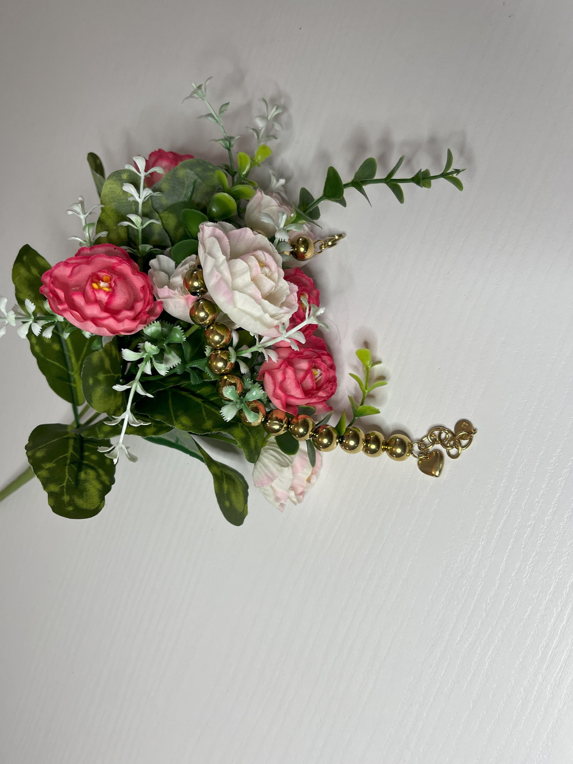 Elegante braccialetto con sfere dorate lucide su fiori bianchi rosa e foglie verdi