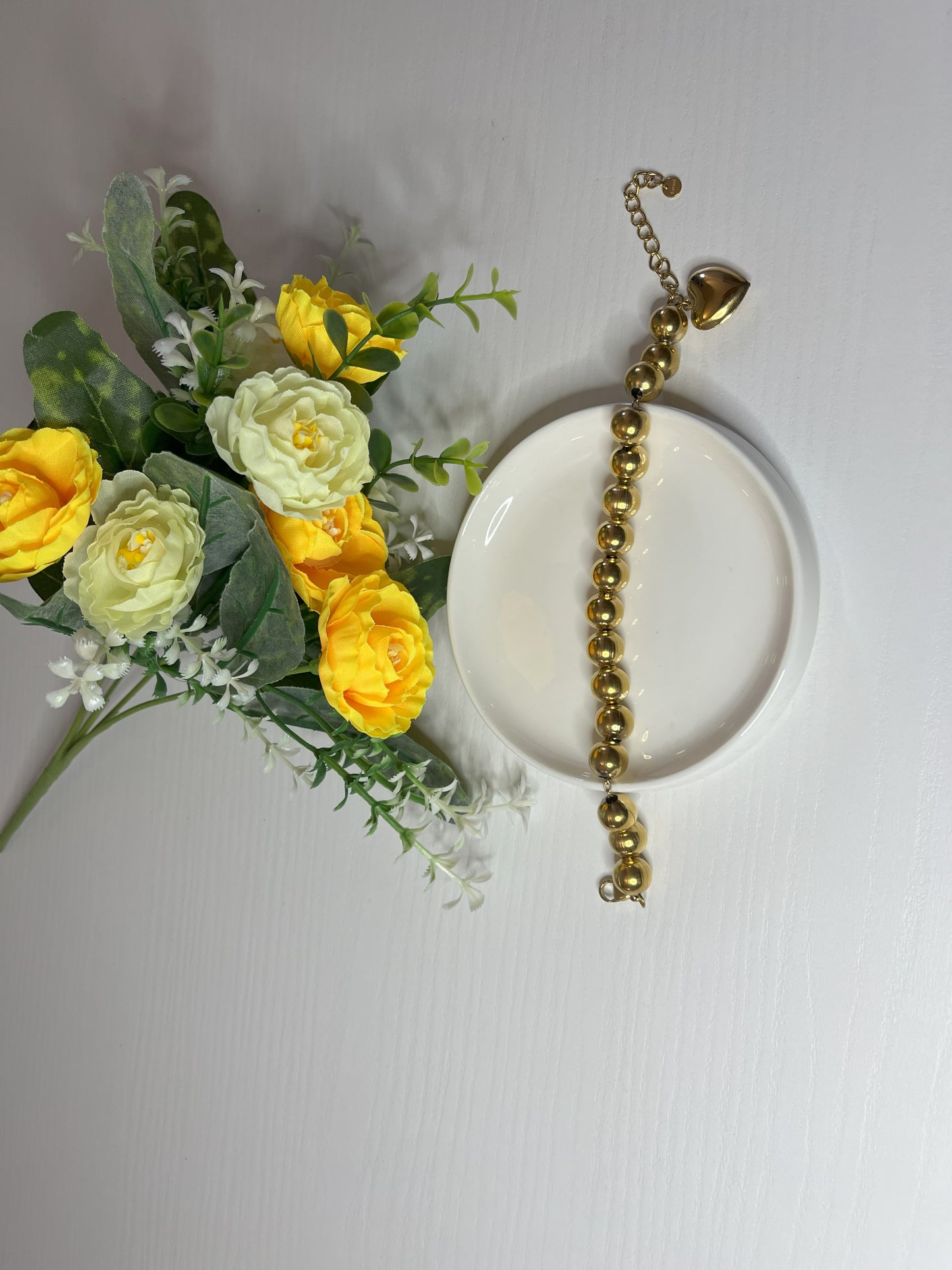 Elegante braccialetto con sfere dorate lucide su fiori gialli e foglie verdi