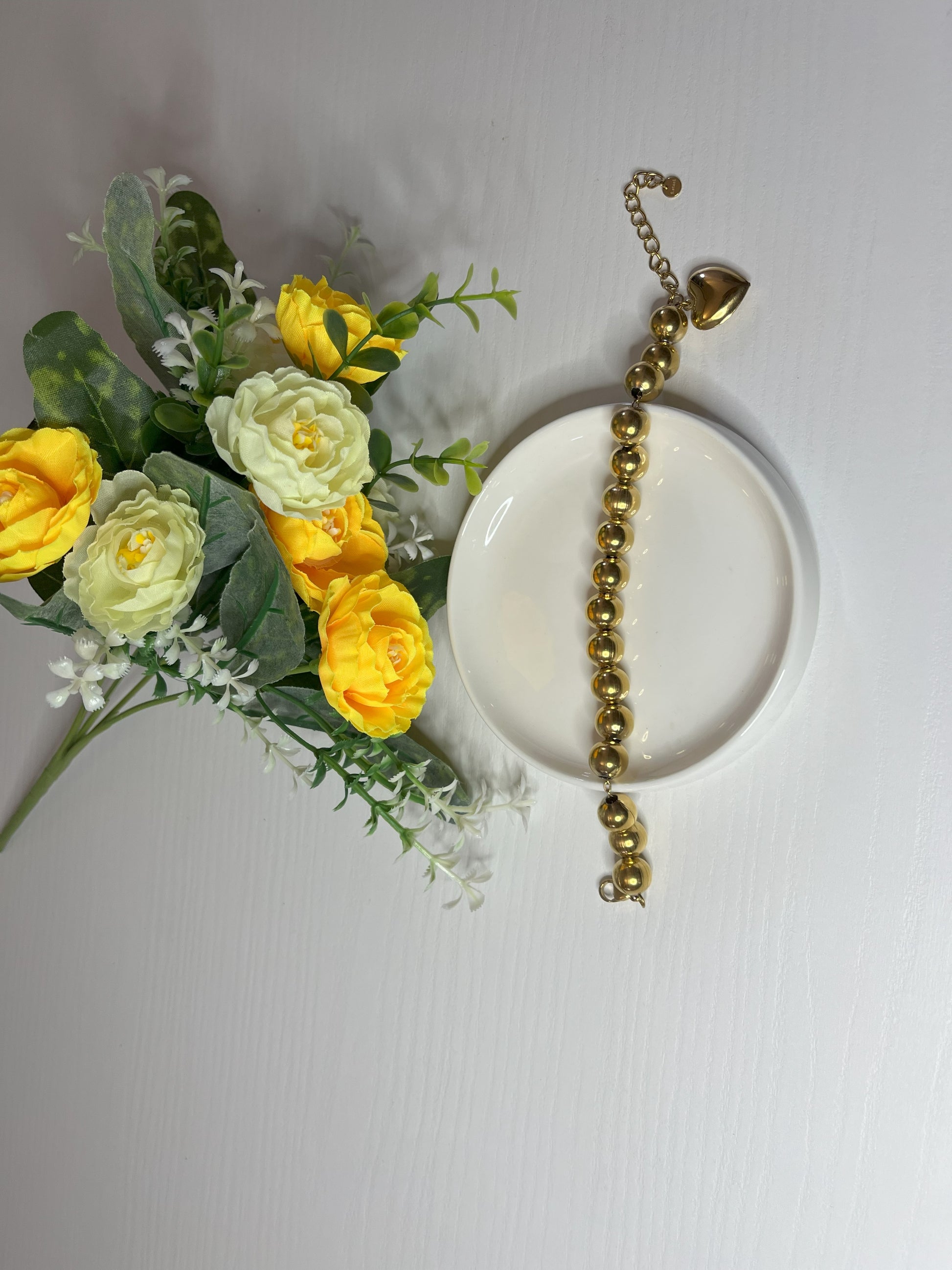 Elegante braccialetto con sfere dorate lucide su fiori gialli e foglie verdi
