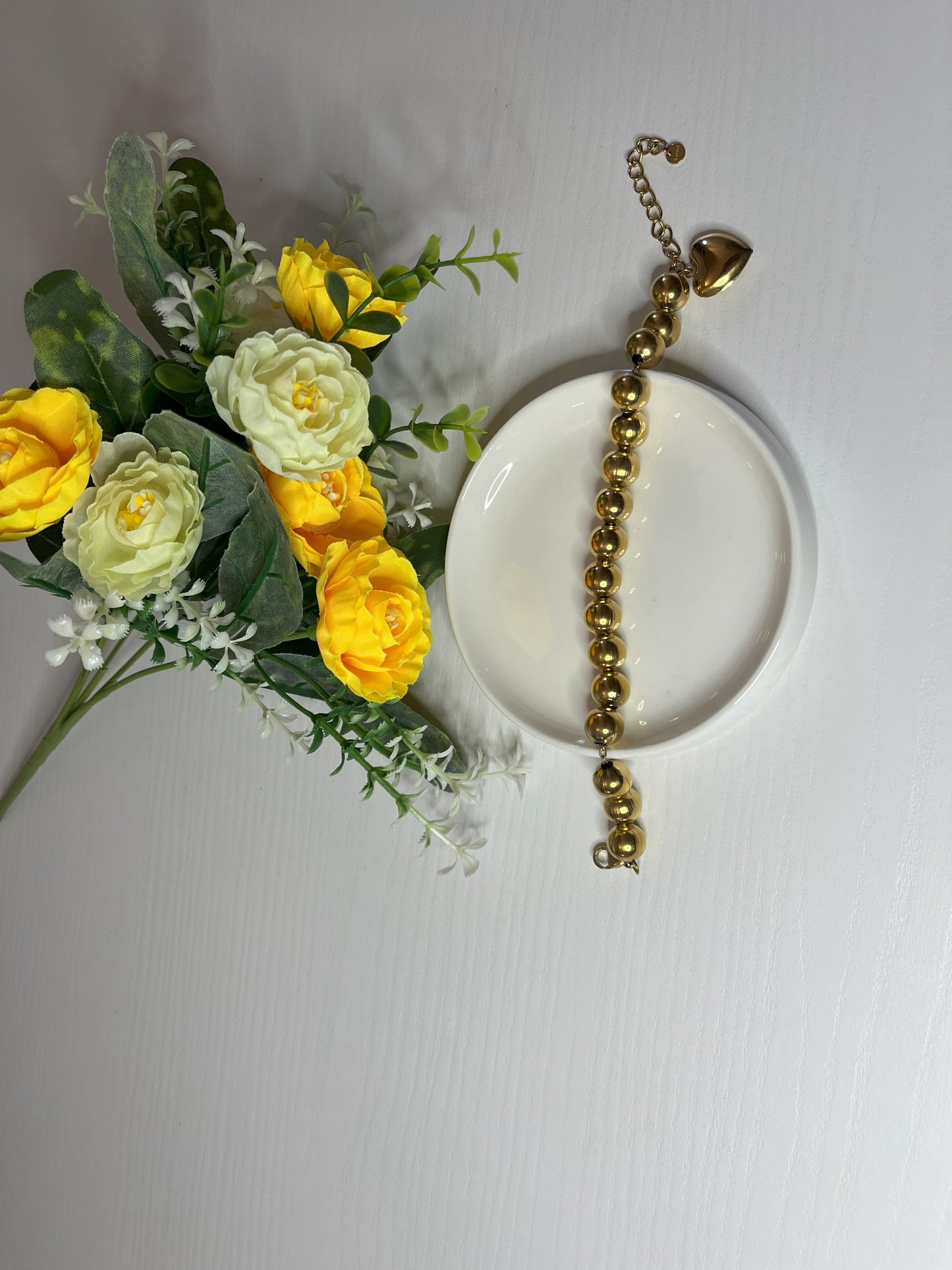 Elegante braccialetto con sfere dorate lucide su fiori gialli e foglie verdi