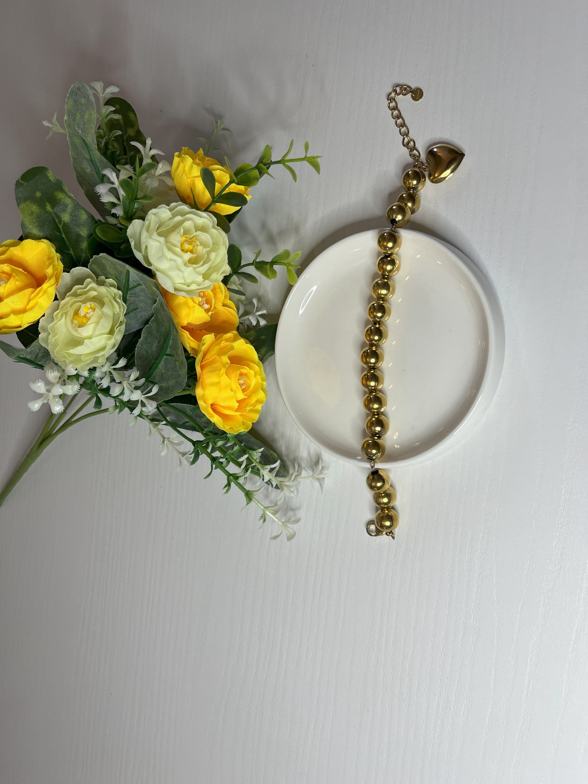 Elegante braccialetto con sfere dorate lucide su fiori gialli e foglie verdi